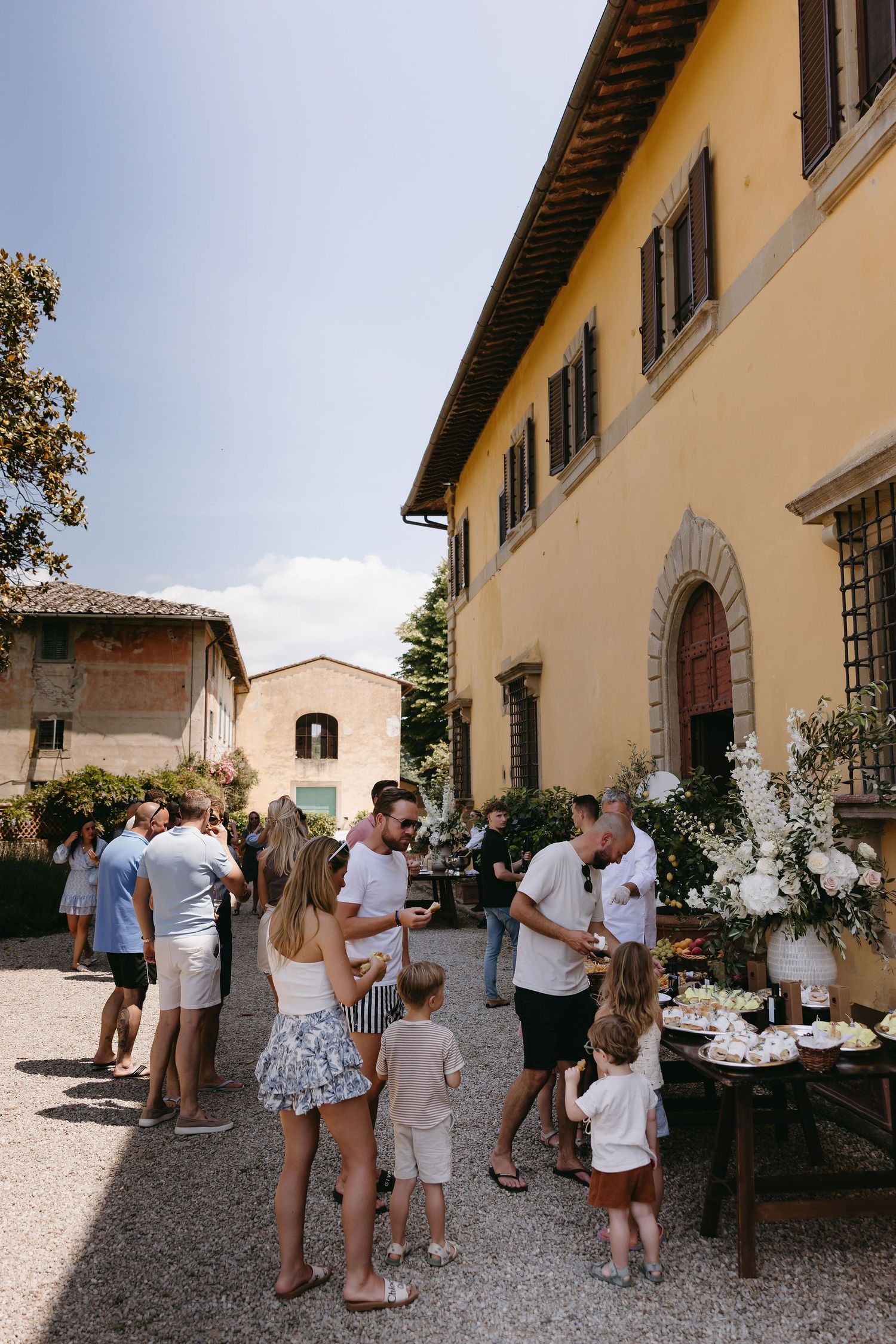 Guests mingling outside a rustic Italian villa during a summer wedding reception.