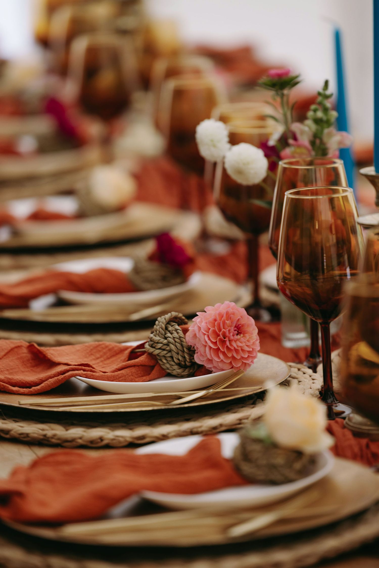 Elegant table setting with coral napkins, wine glasses, and pink floral accents for a special occasion.