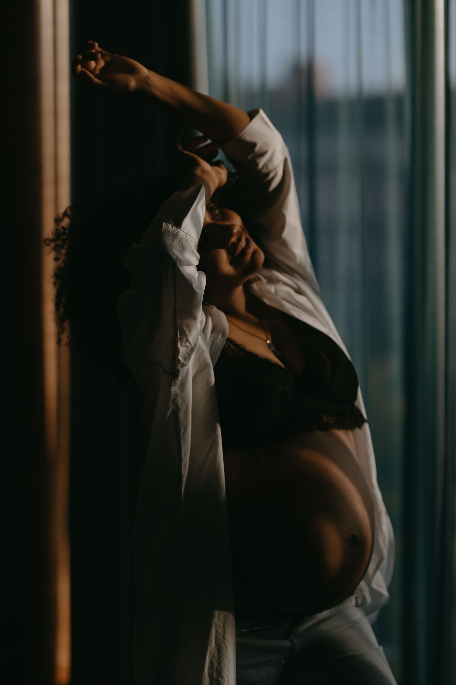 Figure in white clothing poses dramatically against backlit curtains.