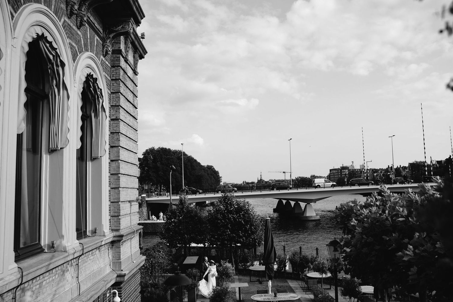 A monochrome vintage photo shows a classical building facade with arches overlooking a highway bridge in the distance.