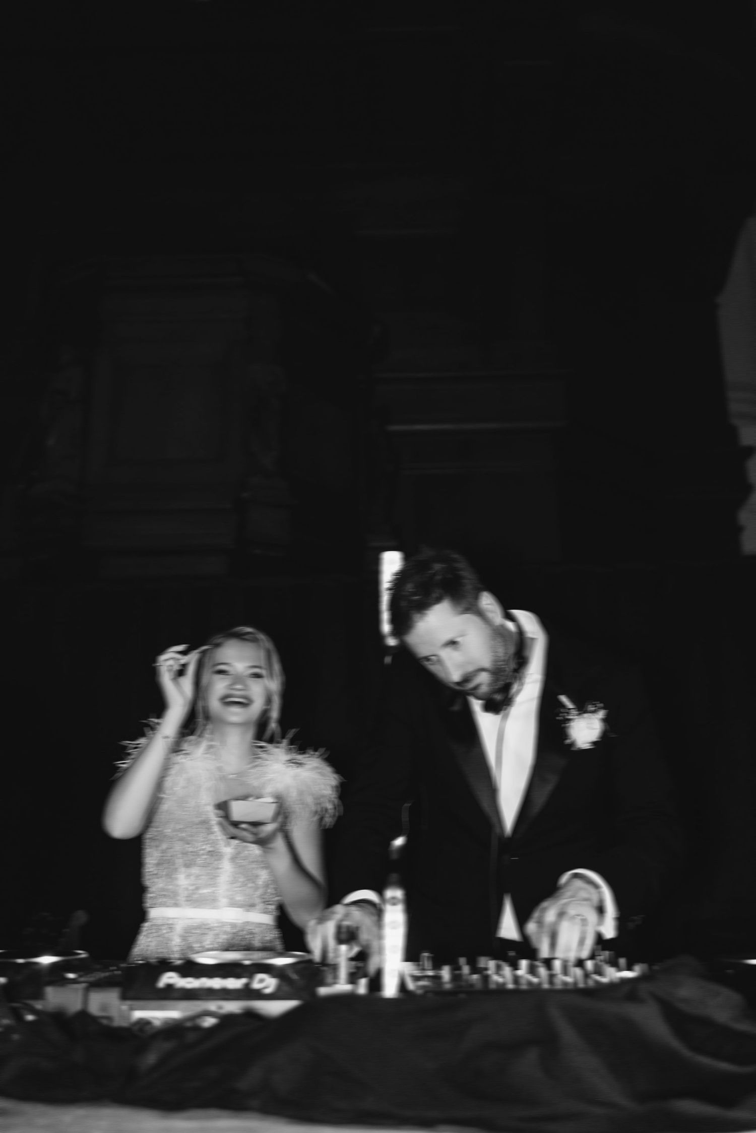 A couple in formal attire DJing together at what appears to be a reception or party.