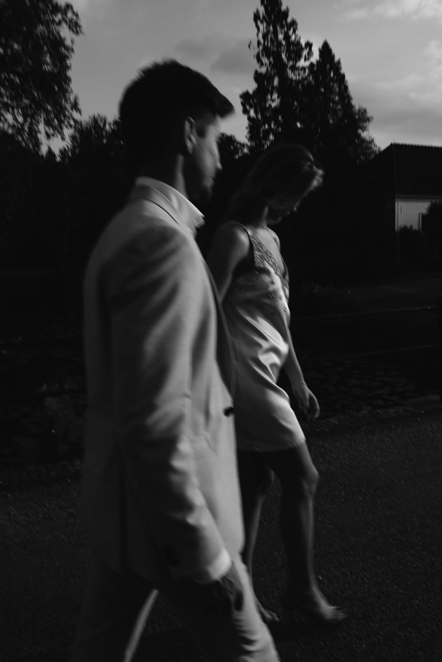 Two figures in white formal attire stand together in silhouette during dusk.