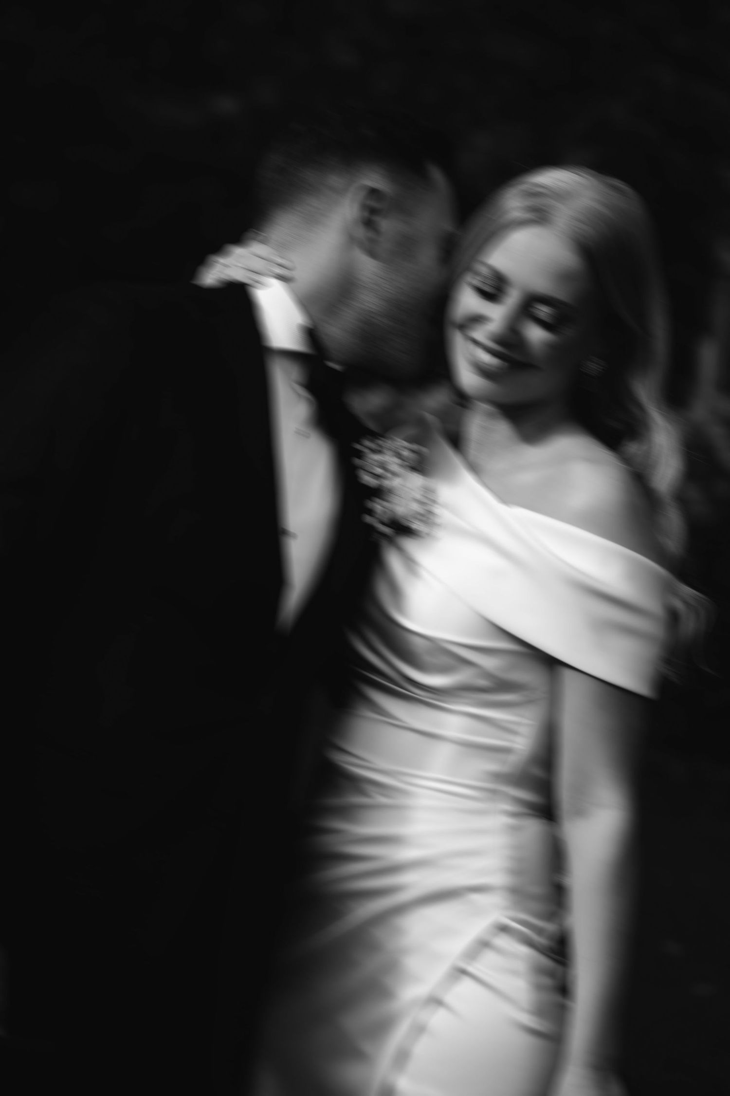 Black and white wedding photo showing a couple dancing, with motion blur capturing an intimate romantic moment.