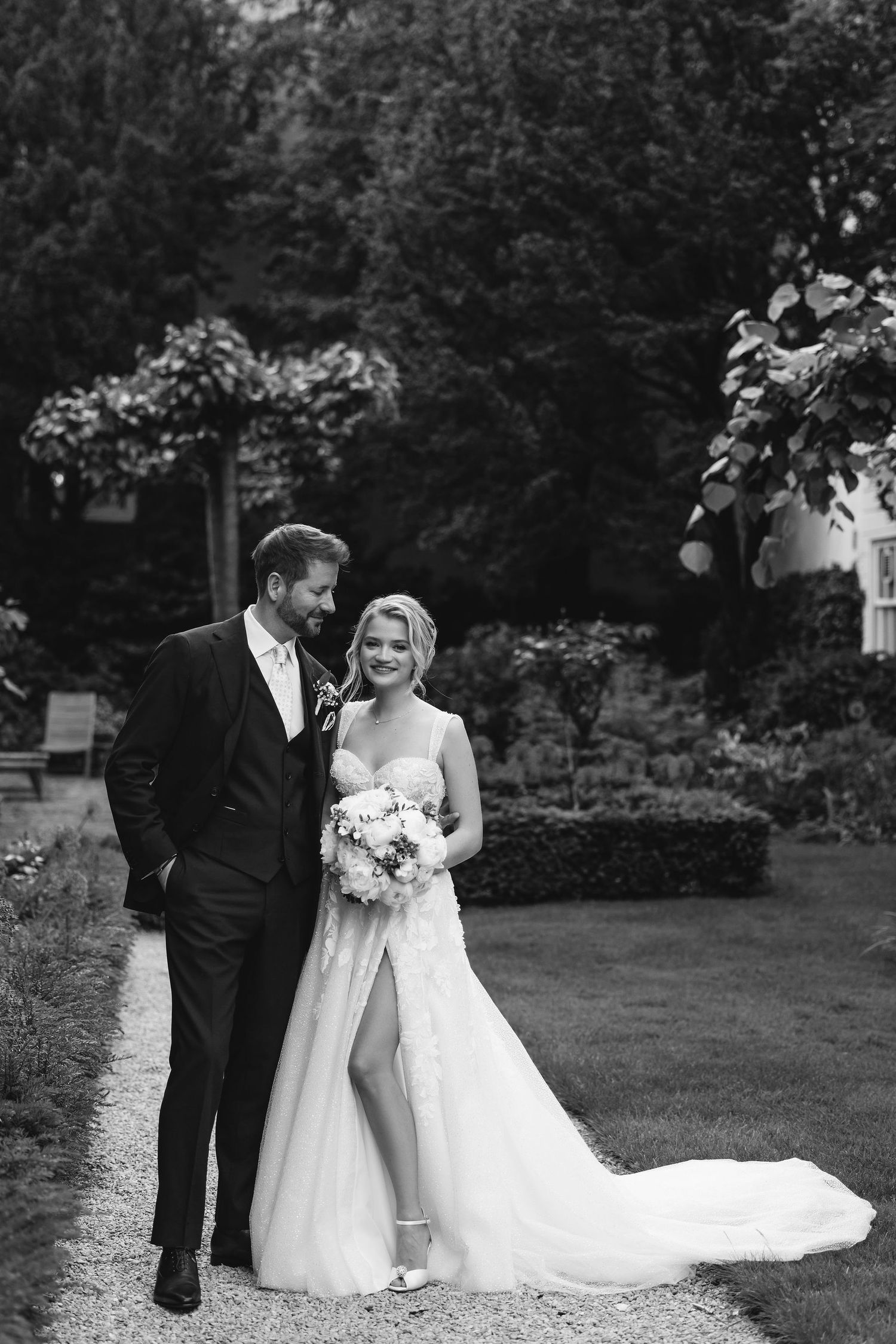 A romantic black and white photo series showing a couple in wedding attire walking through a garden setting.