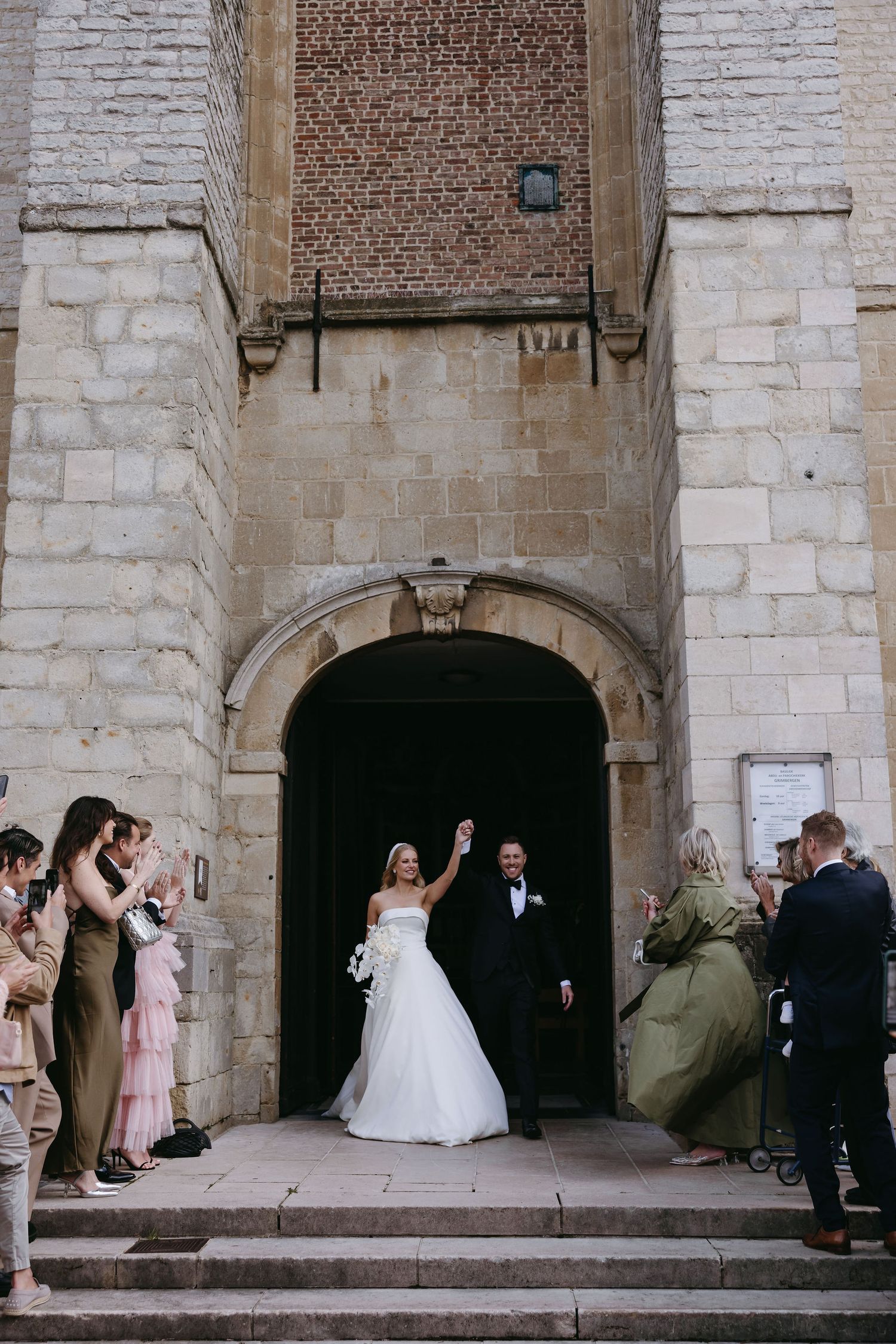 Wedding ceremony exit at historic stone church archway with guests celebrating on steps.