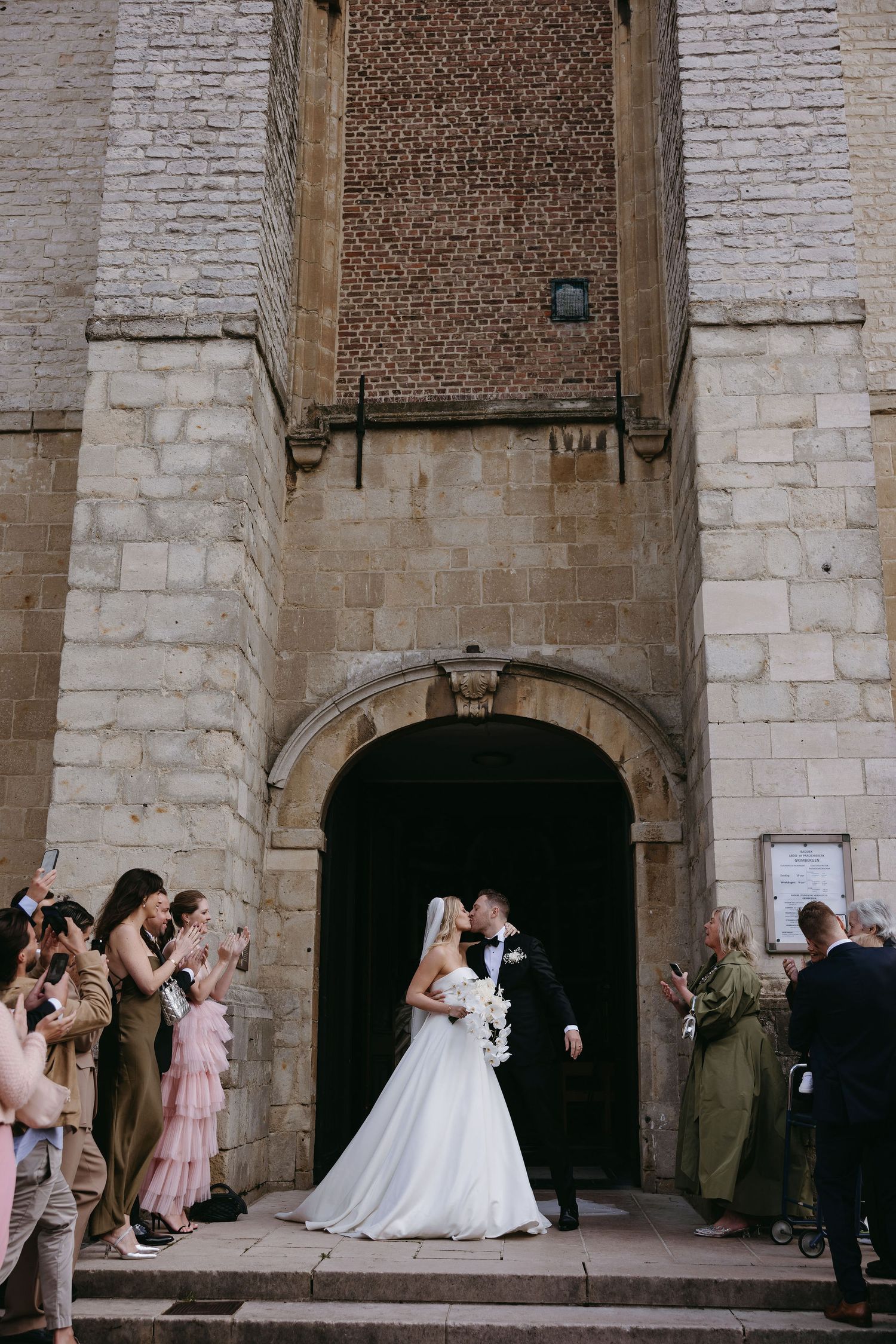 Wedding ceremony under historic stone archway with guests watching from either side.