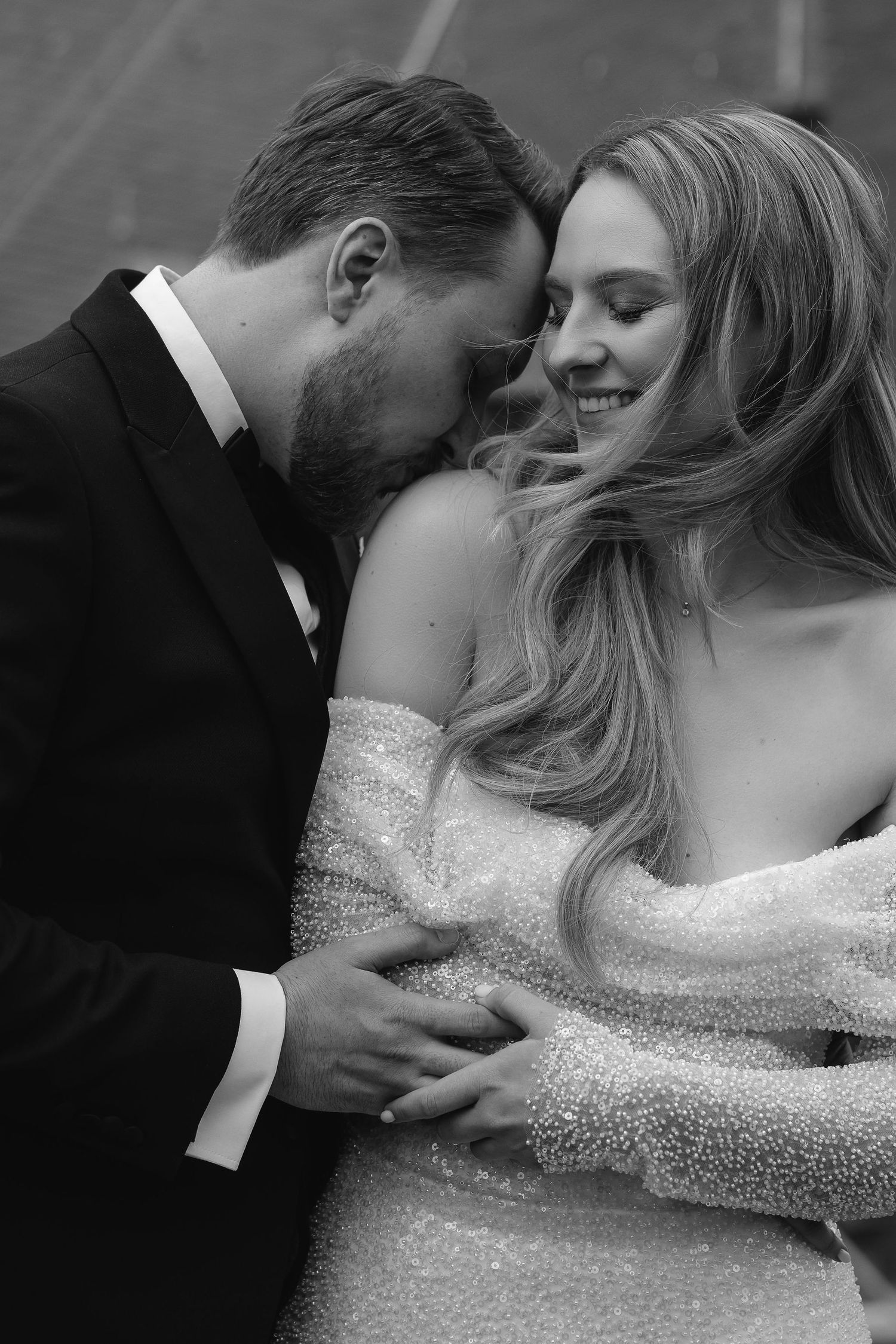 Intimate black and white portrait of newlyweds sharing a tender moment in formal wedding attire.