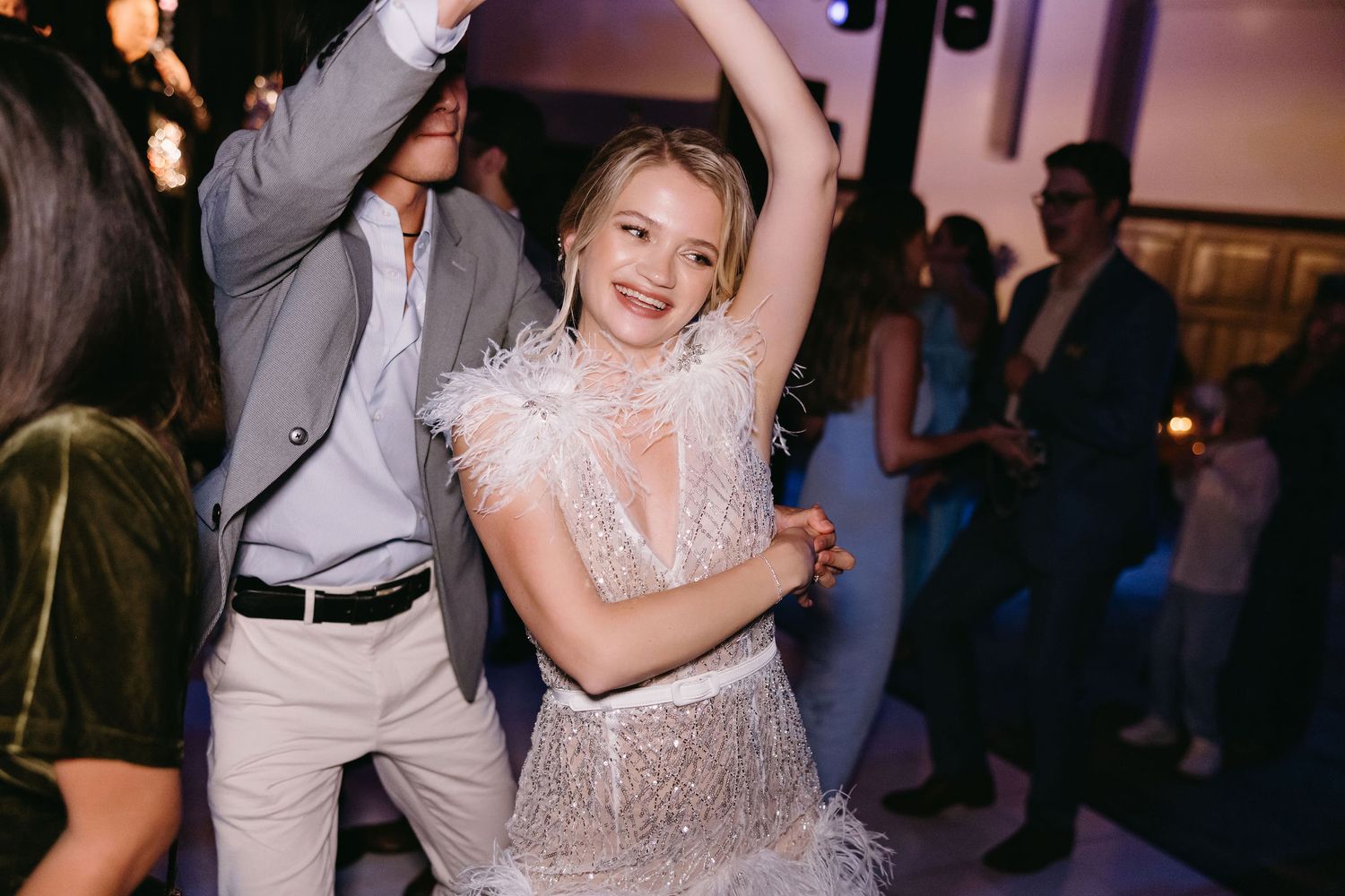 People dancing and celebrating at a wedding reception with atmospheric lighting.
