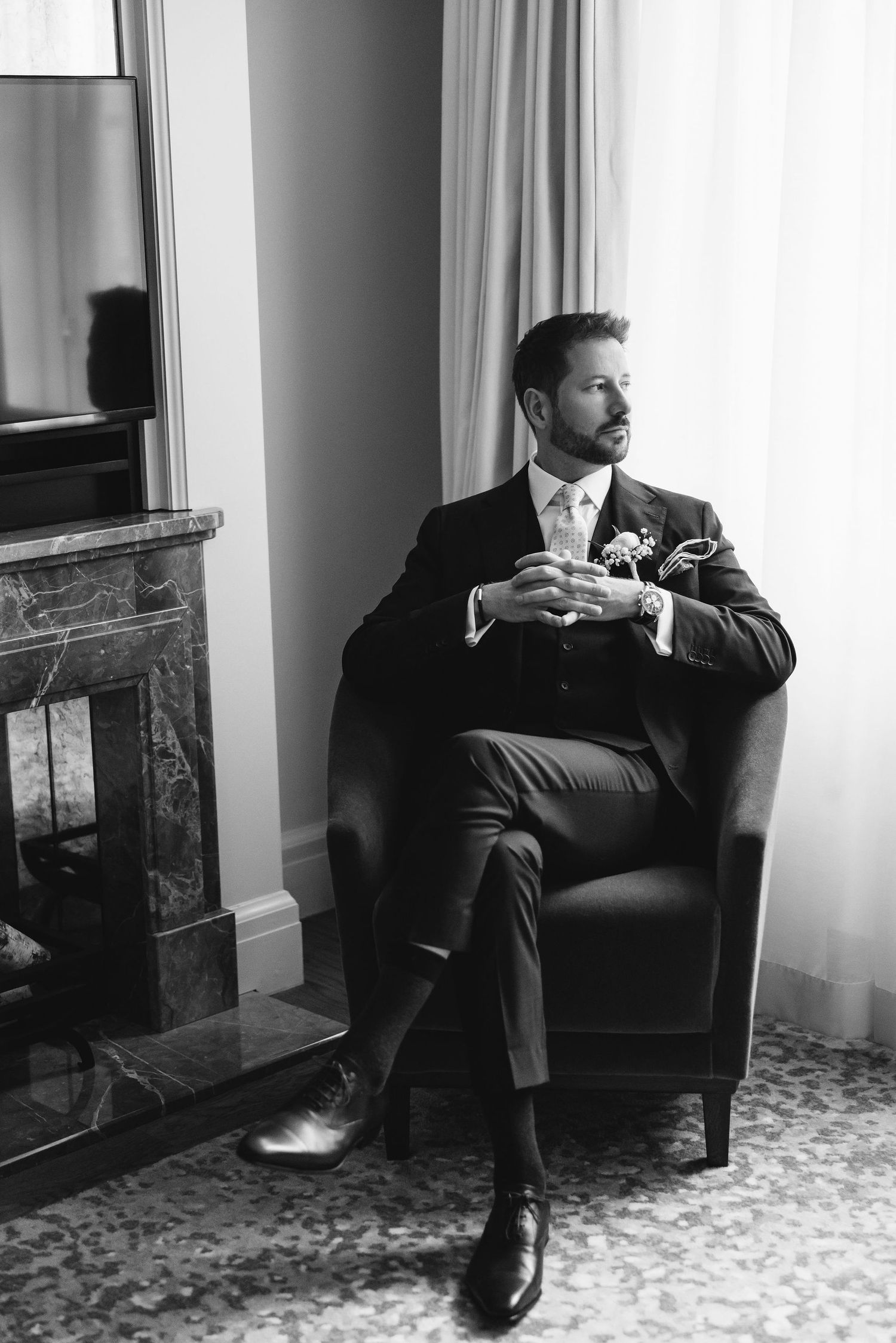Classic black and white portrait of person in suit sitting pensively by window.