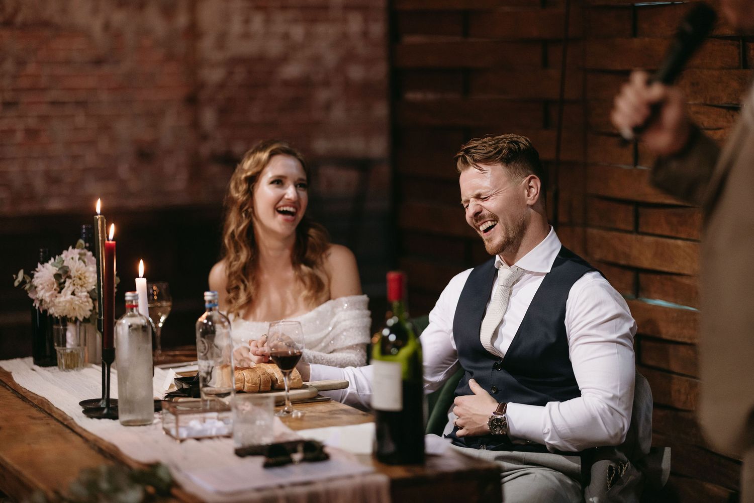 A couple shares a romantic moment at an intimate dinner table in a rustic brick-walled restaurant.