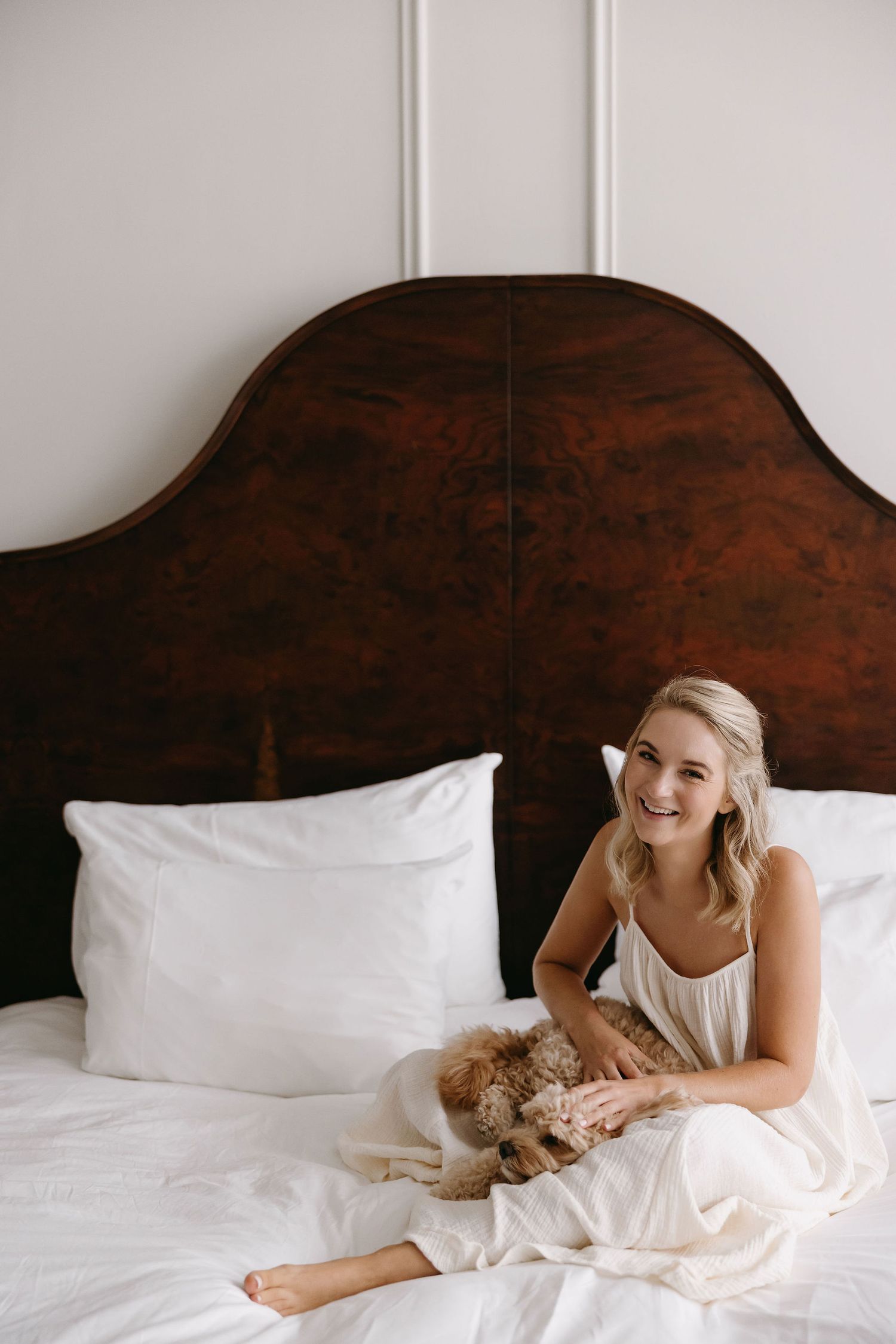 A person in white lounges on a bed with dark wooden headboard.