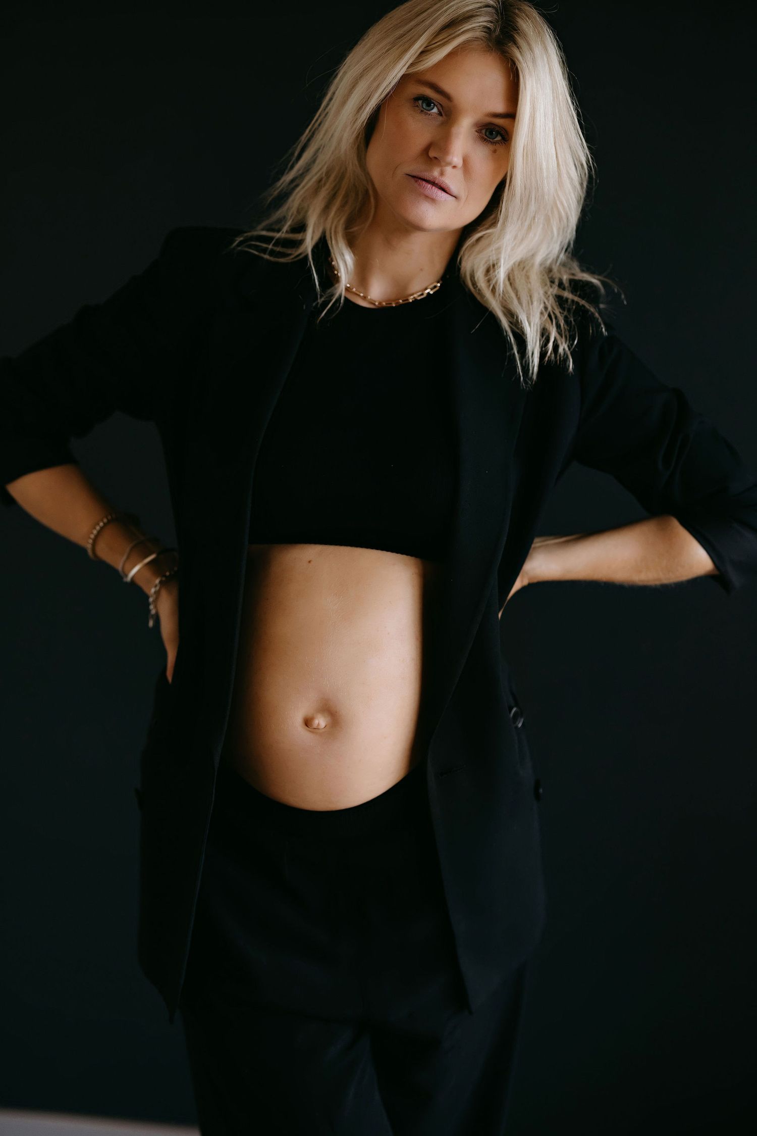 Dramatic maternity photos in black outfit against dark background.