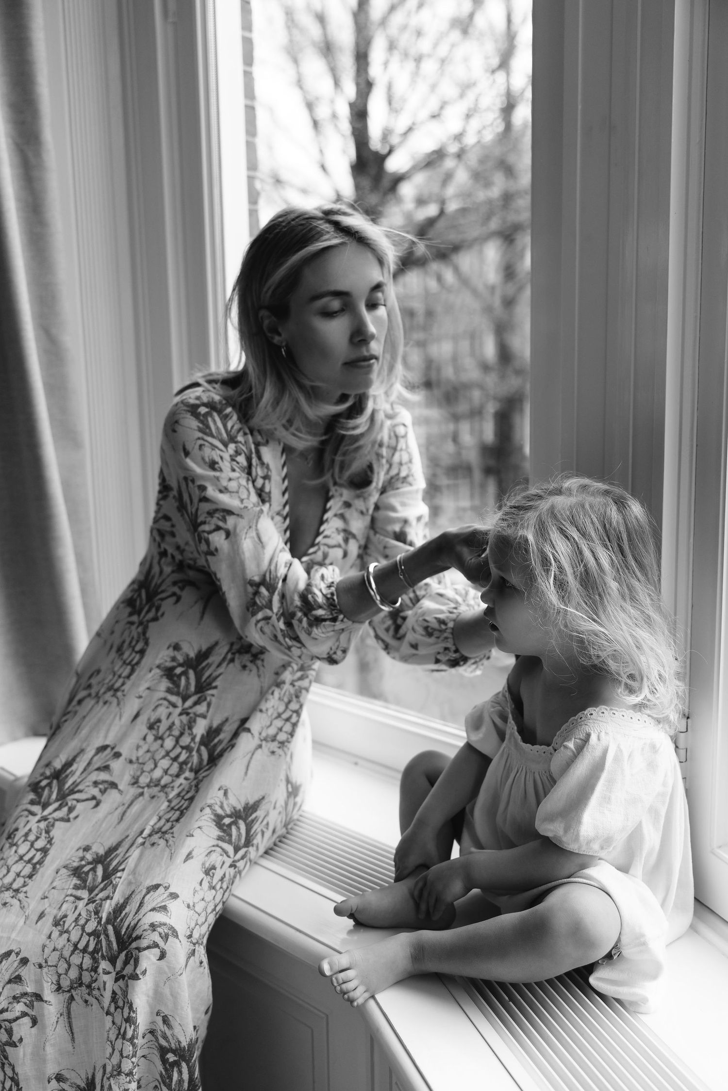 Black and white photo of intimate family scene by window.