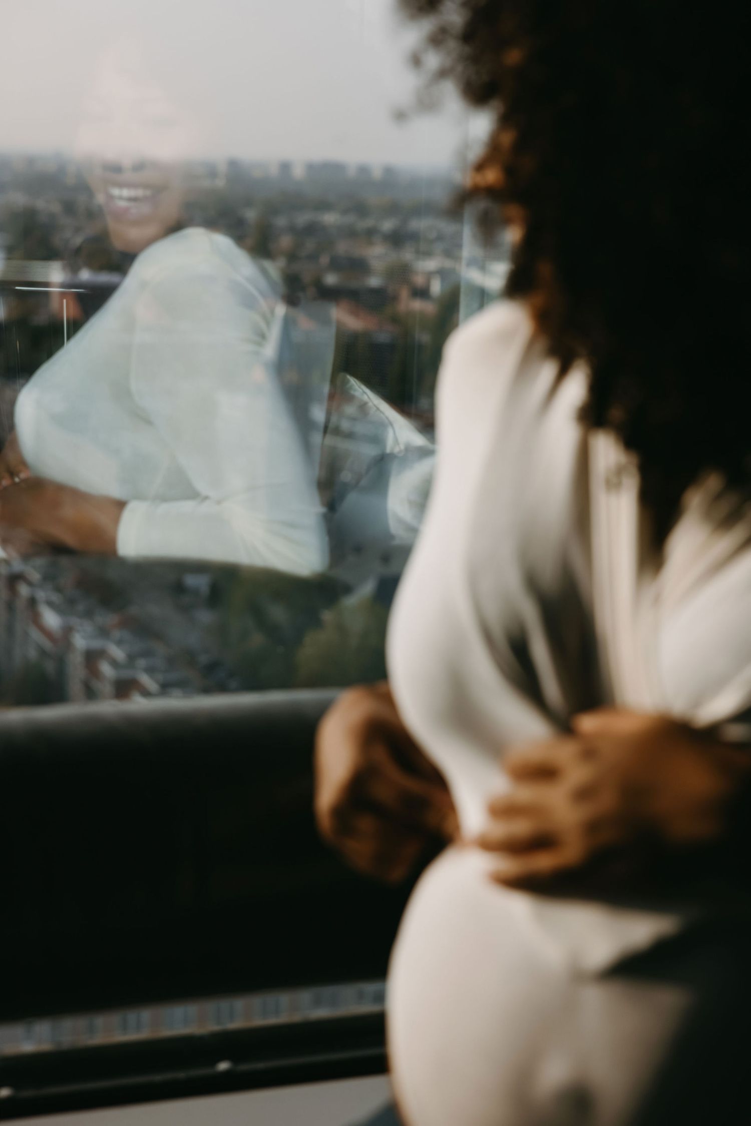Artistic maternity photo with reflections in window overlooking city view.