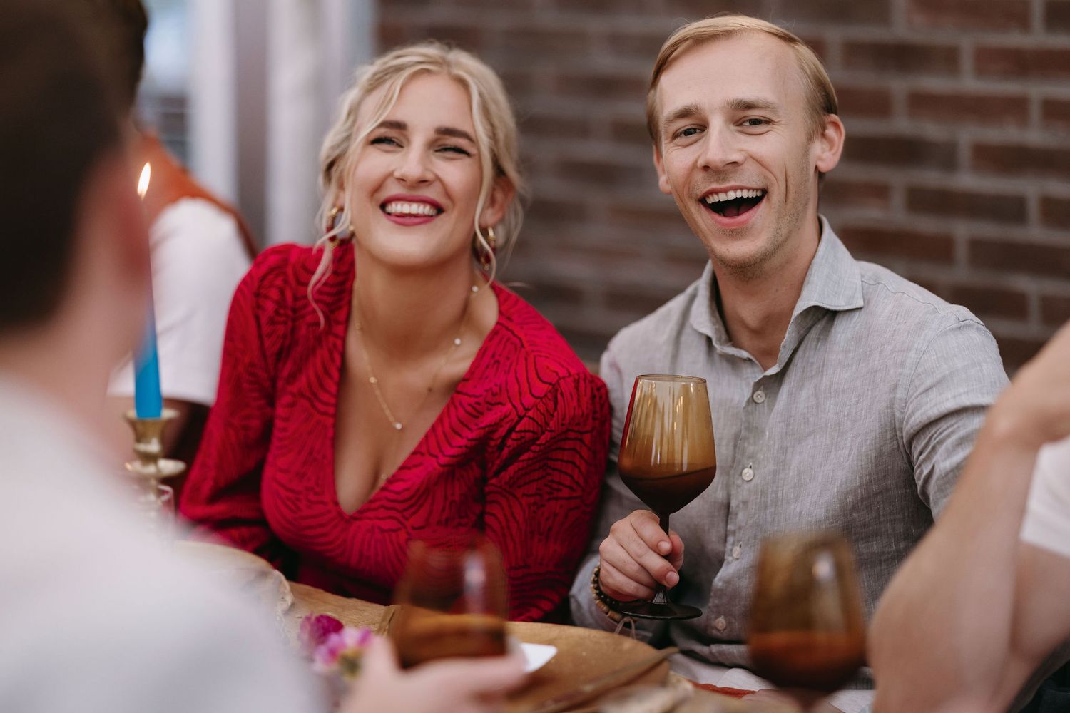 Wedding guests enjoying conversation and laughter at a reception with brick wall background.
