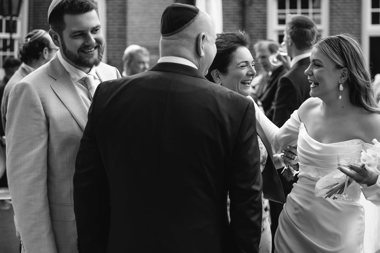 A candid black and white photo capturing a joyous wedding celebration outdoors with guests.