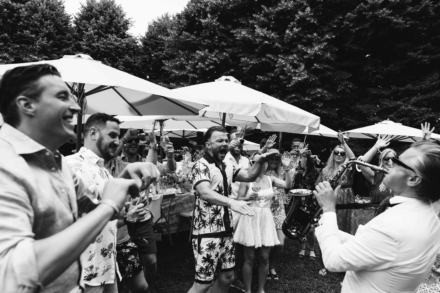 Black and white photo of wedding guests celebrating with champagne under outdoor umbrellas.