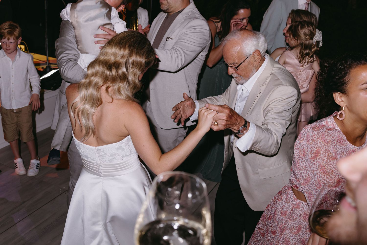 Wedding guests dancing together on a brightly lit dance floor during an evening celebration.