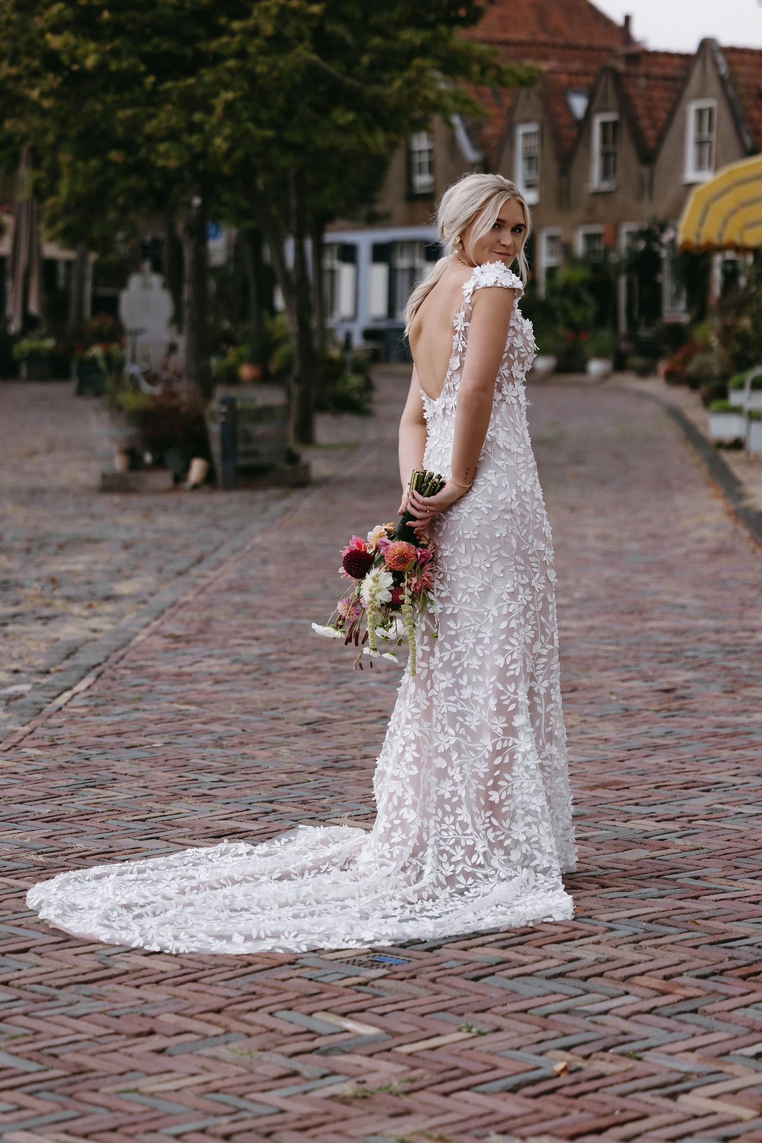 Bride in intricate lace wedding gown with long train poses on cobblestone street.