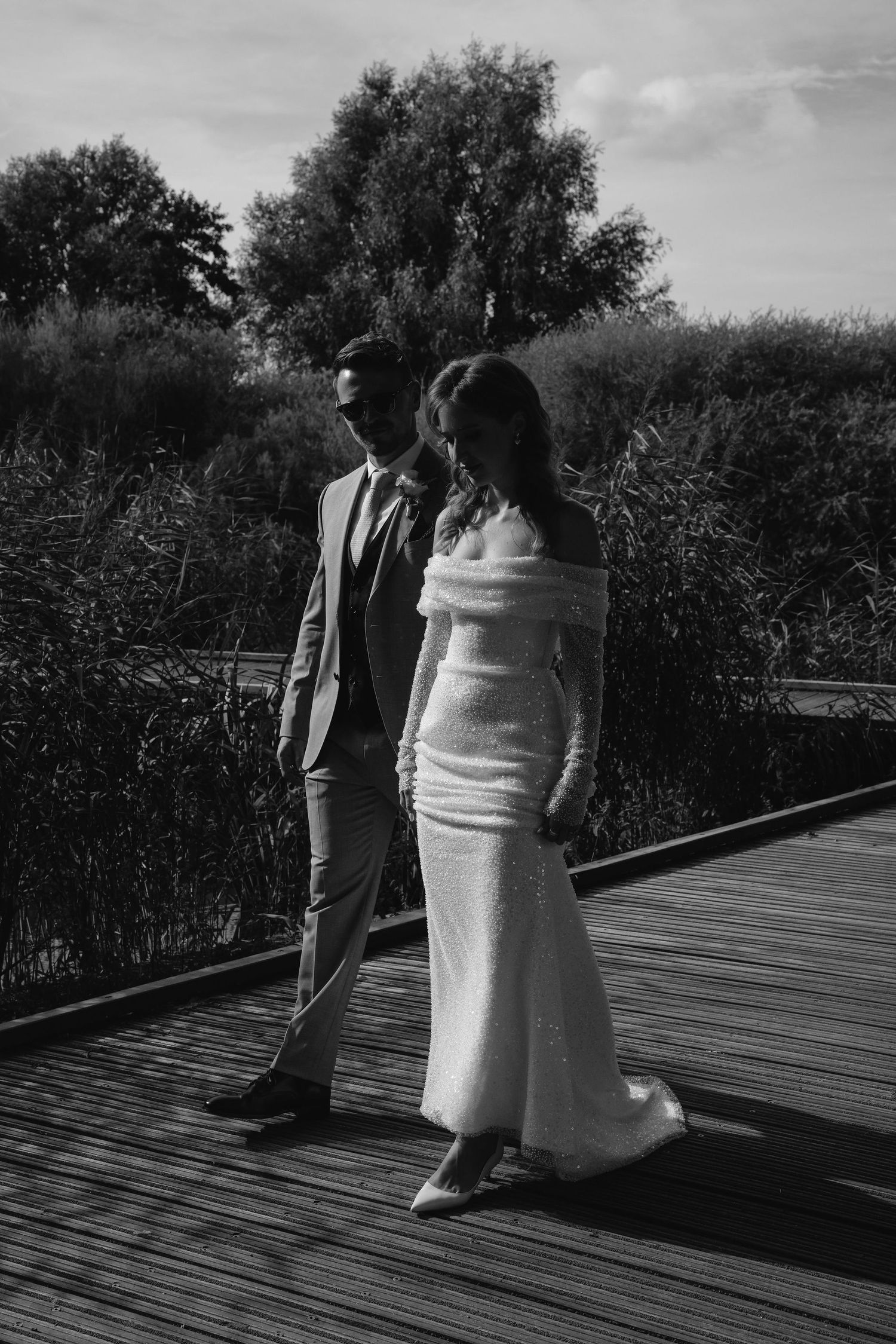 Black and white photo of two people standing on a wooden deck surrounded by foliage.
