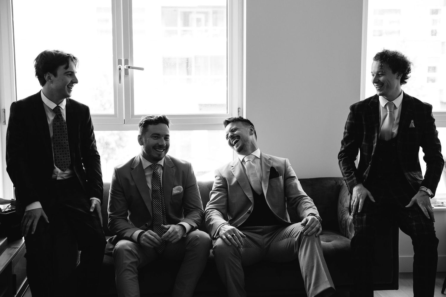 Silhouetted wedding party preparing by windows in formal attire.