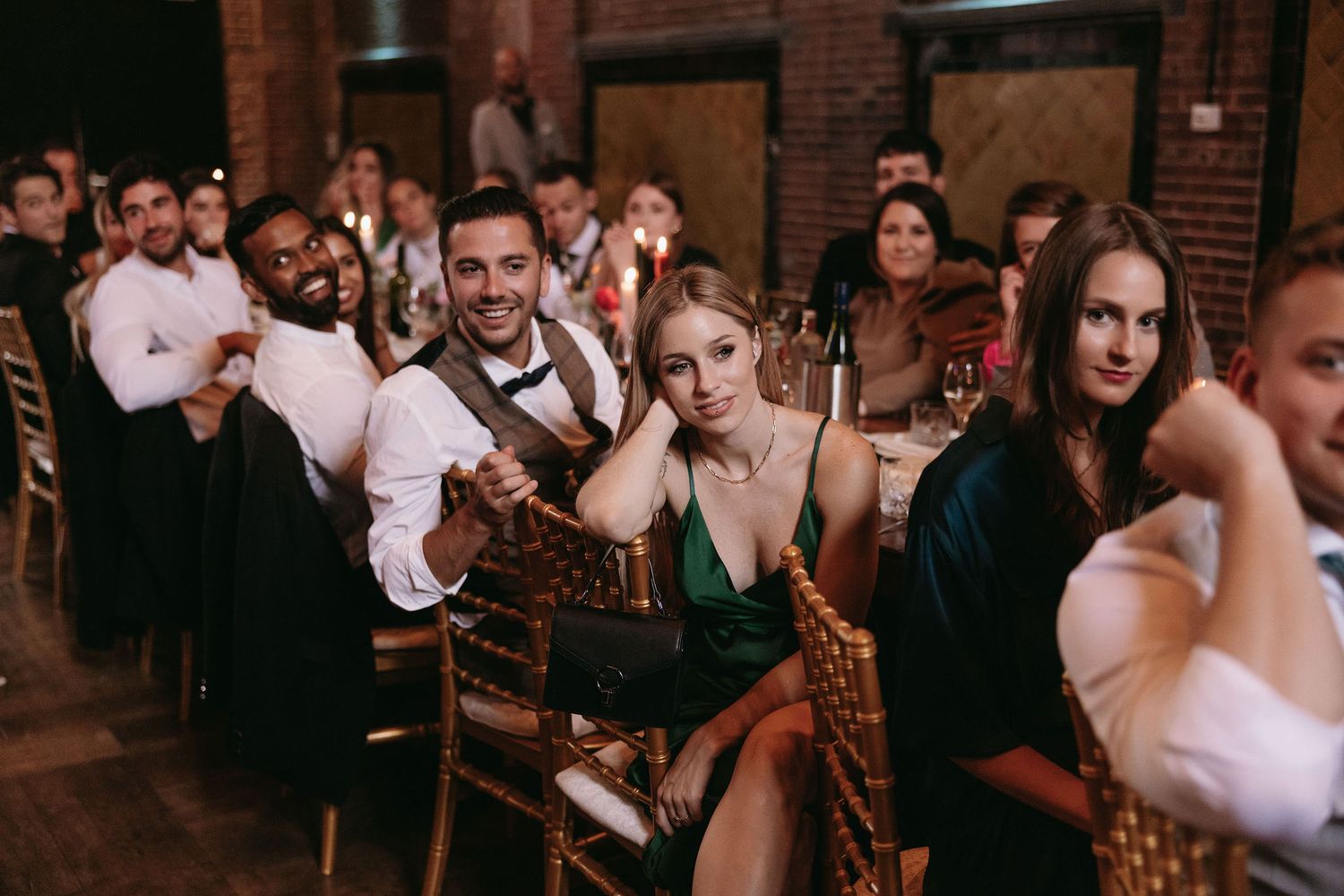 Guests seated at wedding reception tables in an industrial brick venue with warm lighting.