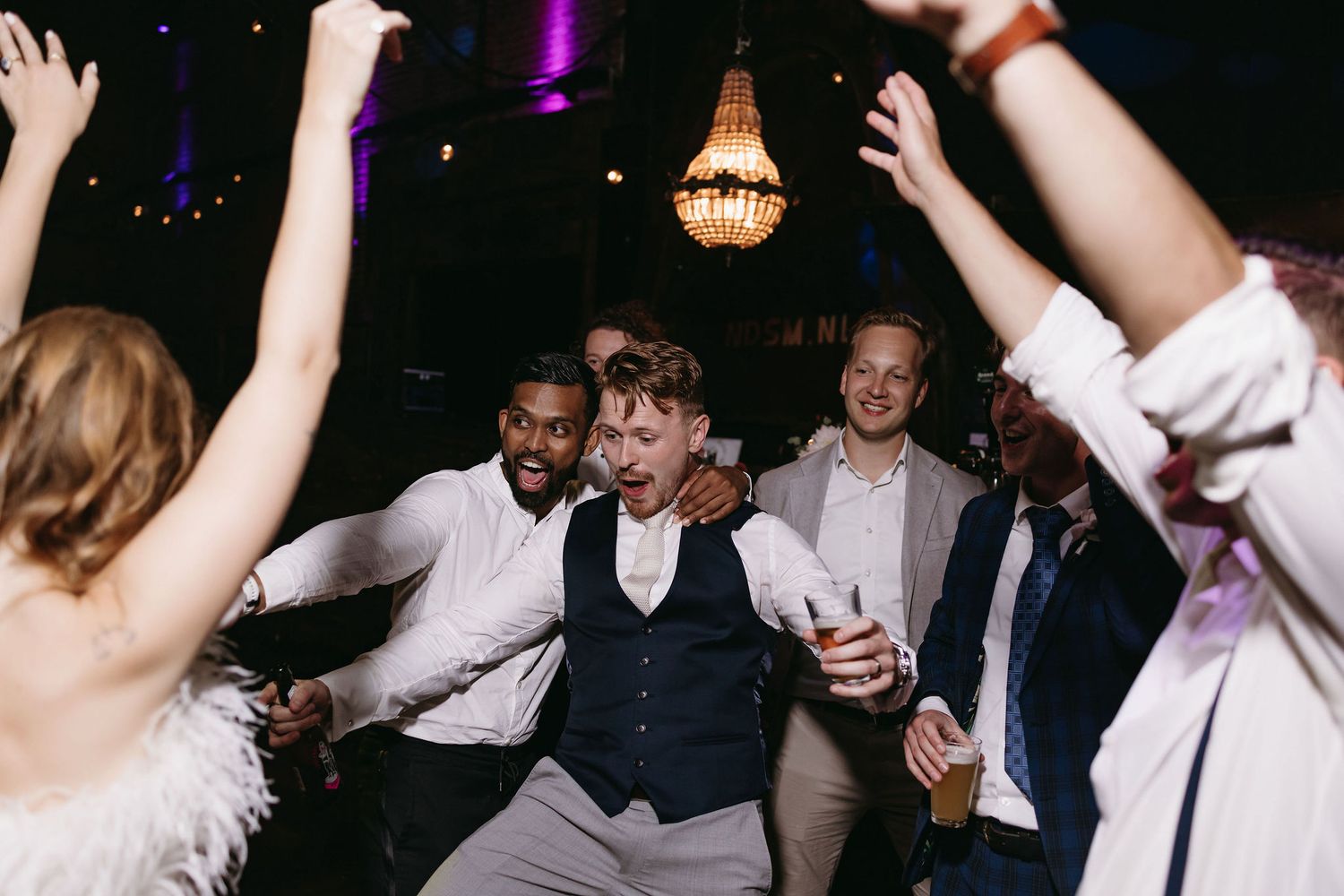 Wedding guests dancing joyfully on a dark dance floor illuminated by purple lighting.