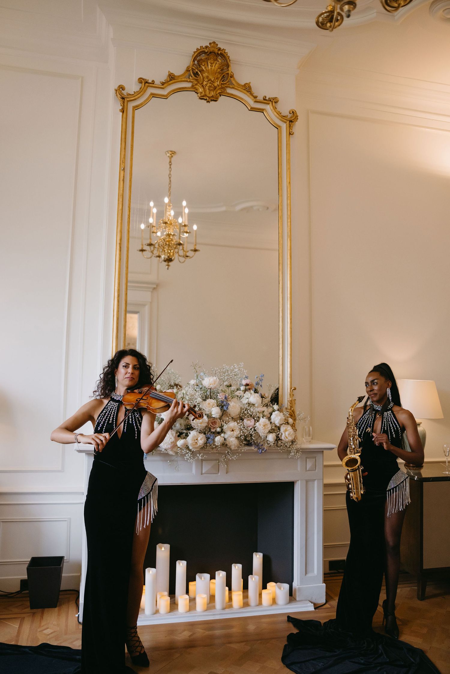 Musicians performing with violin in formal black attire beside an ornate gold mirror.