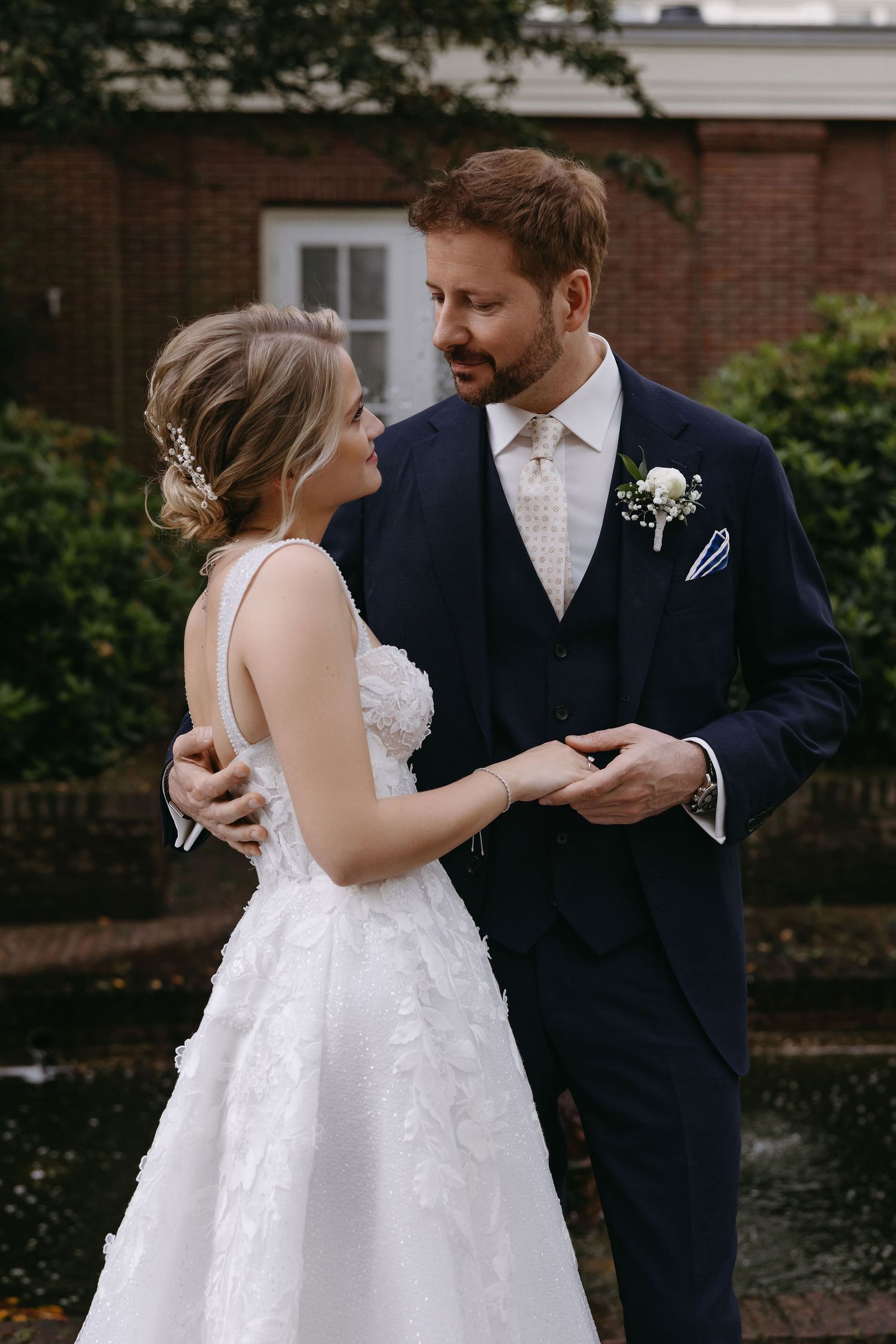 Intimate wedding portrait showing couple in formal attire against brick building backdrop.