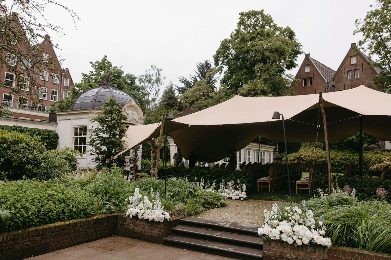 Outdoor wedding venue with beige tent, white floral arrangements, and manicured gardens.