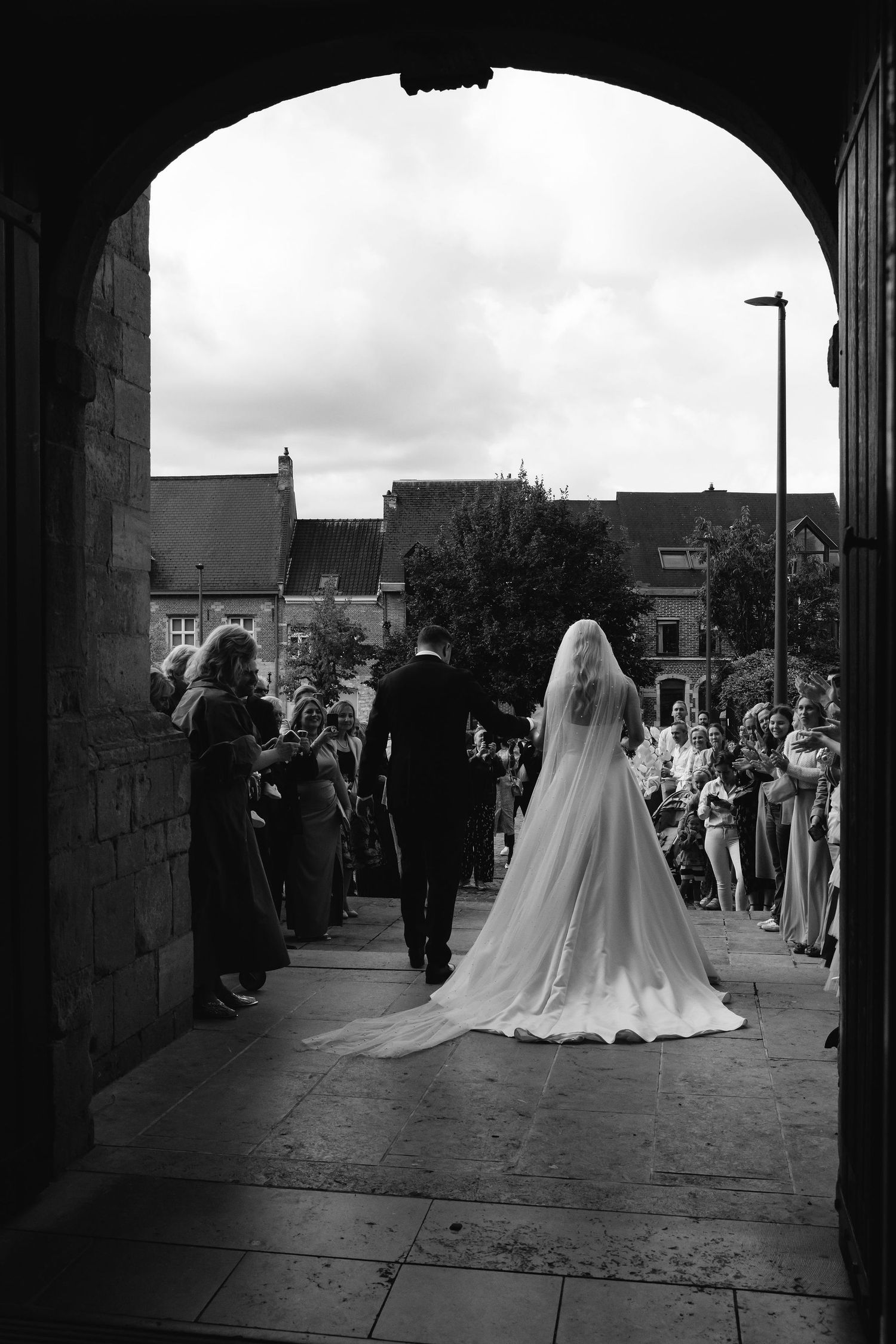 A dramatic black and white shot of a wedding processional through a stone archway.