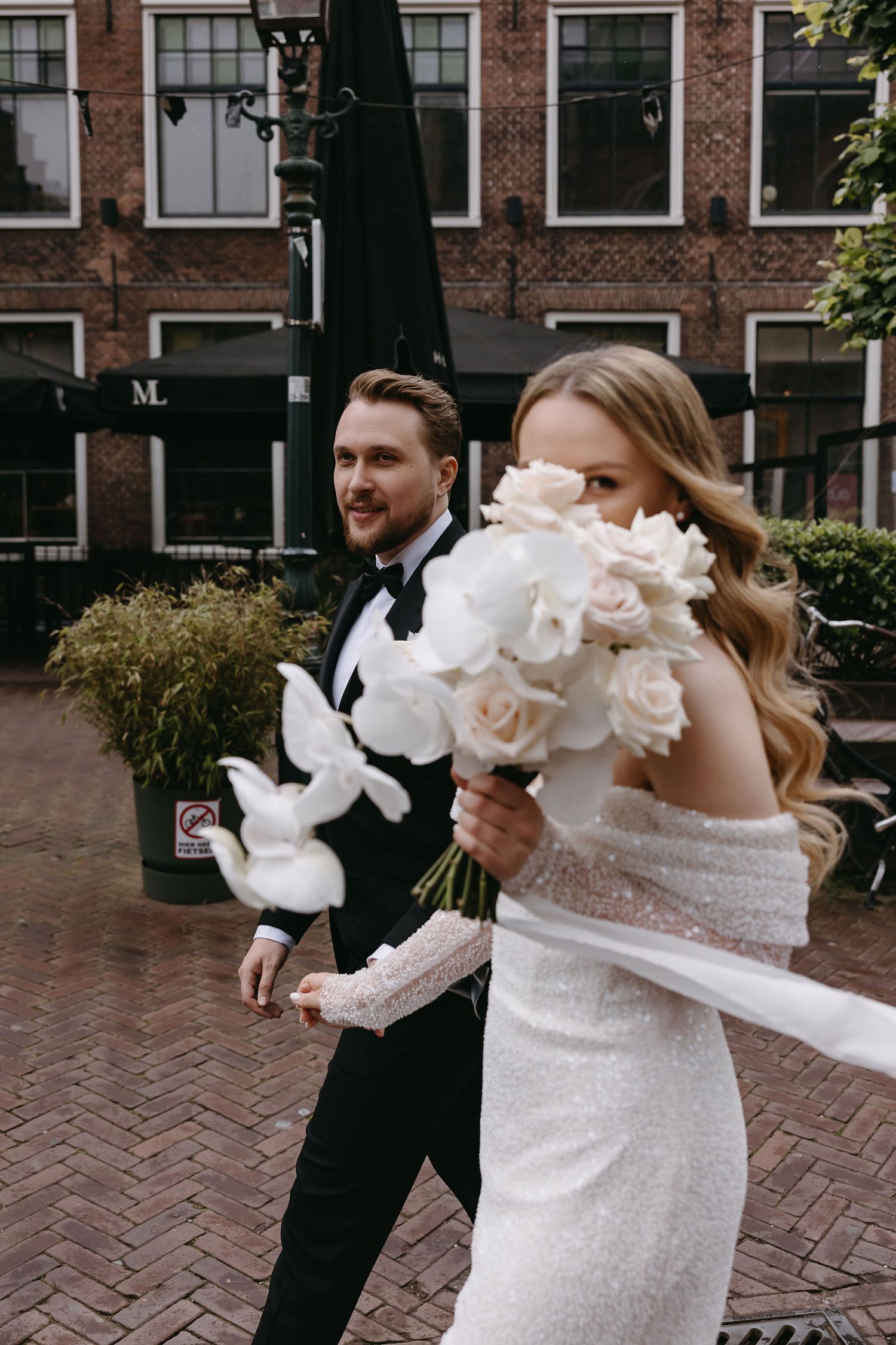 A festive wedding moment captured on a brick-paved street with white floral bouquets.