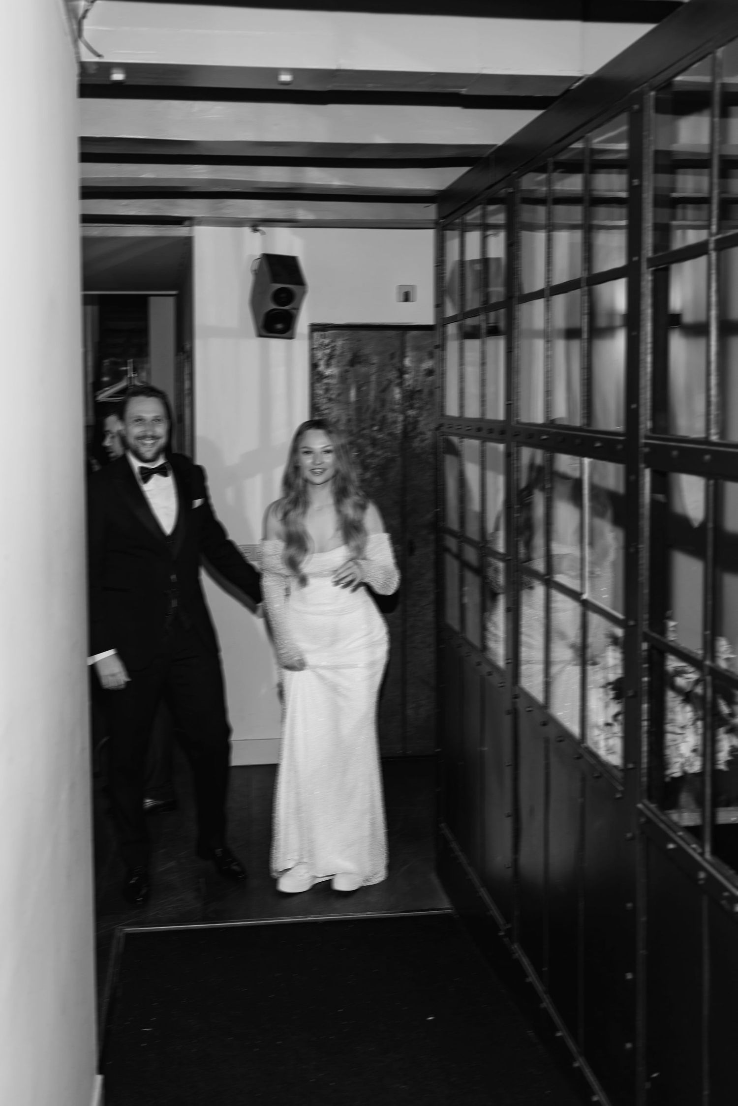 Joyful couple walking through an elegant corridor with exposed beams and glass walls.
