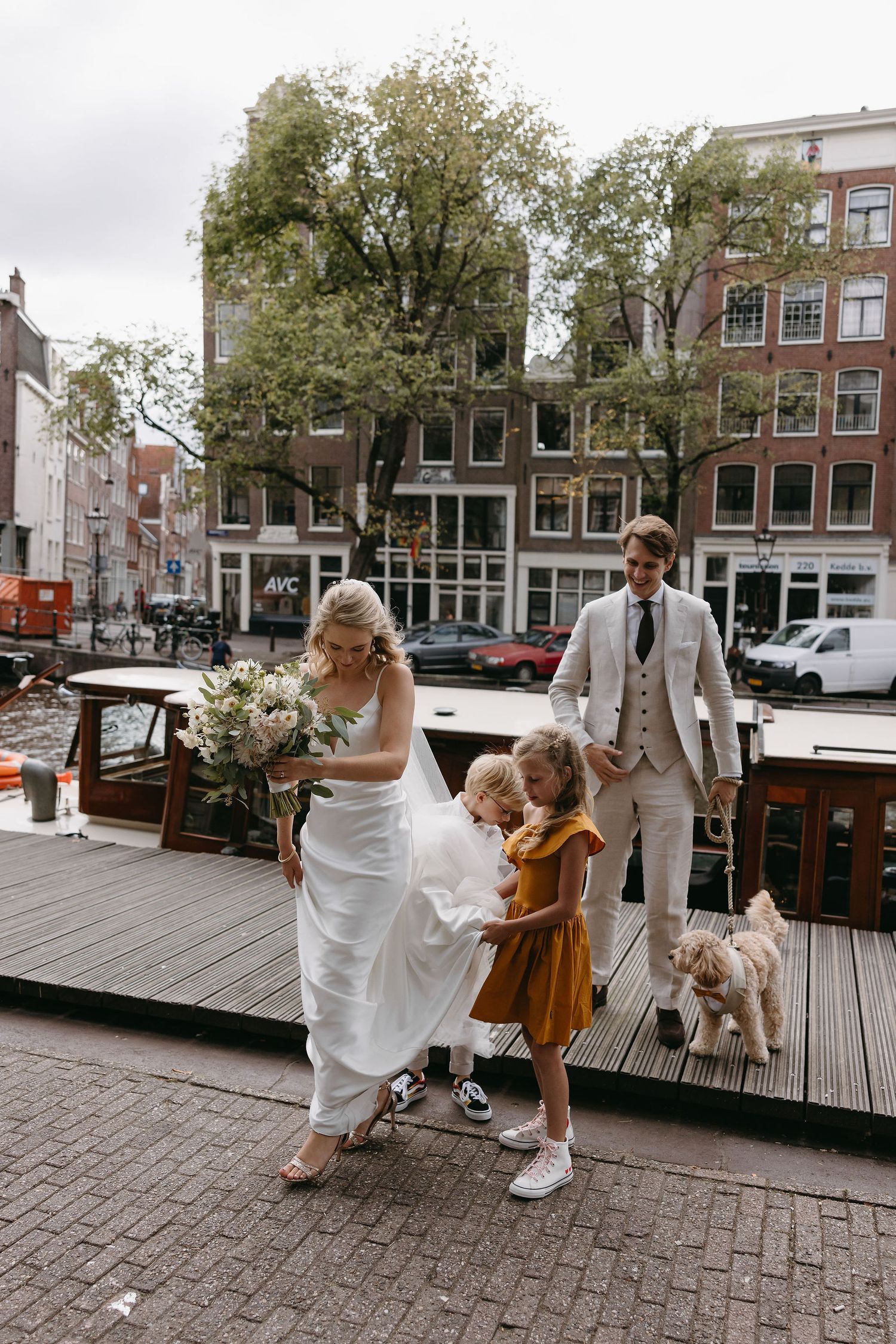 Wedding party celebrating on a canal-side dock with historic buildings in the background.