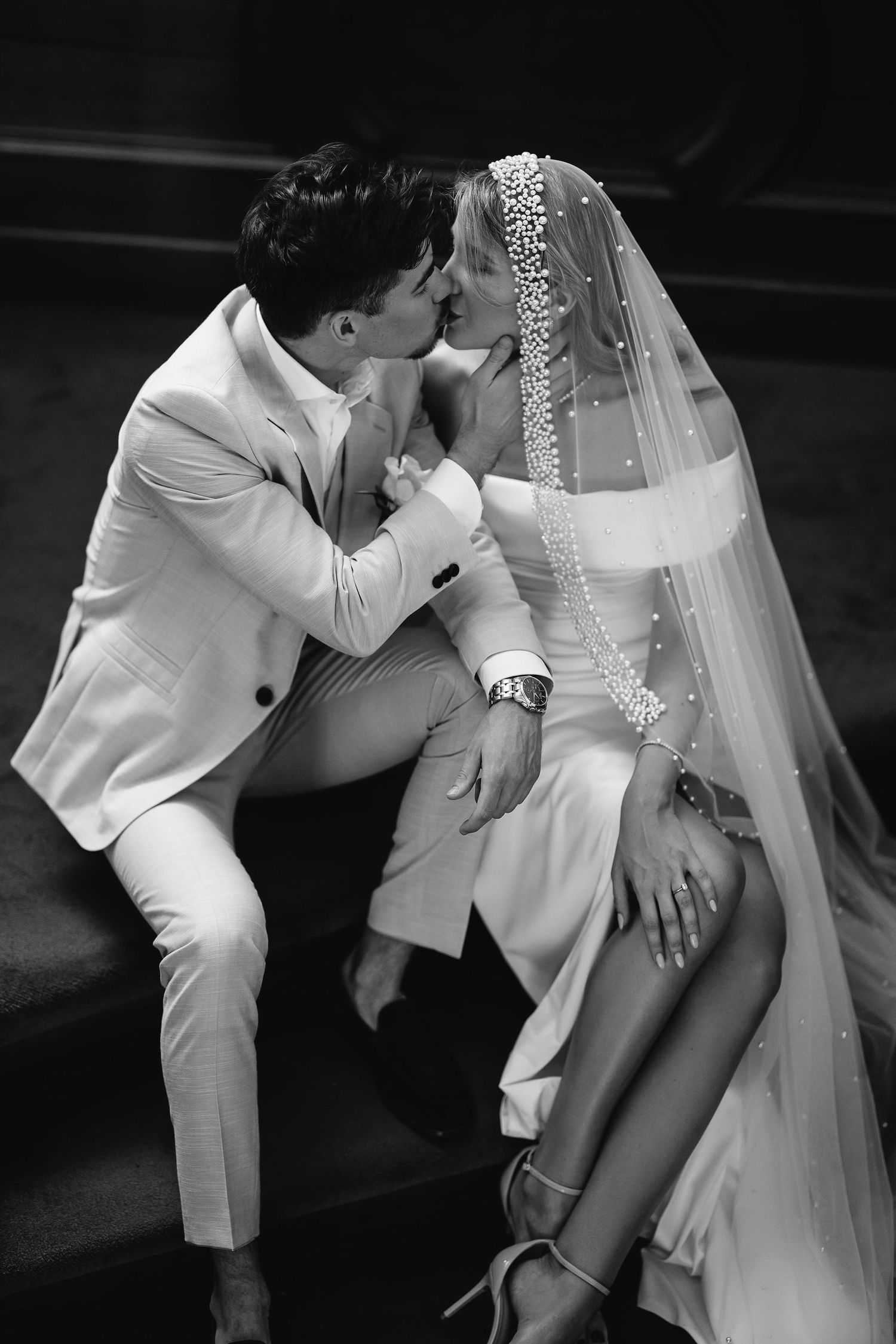 Intimate black and white wedding photo showing couple in elegant white attire and veil sharing a romantic moment.