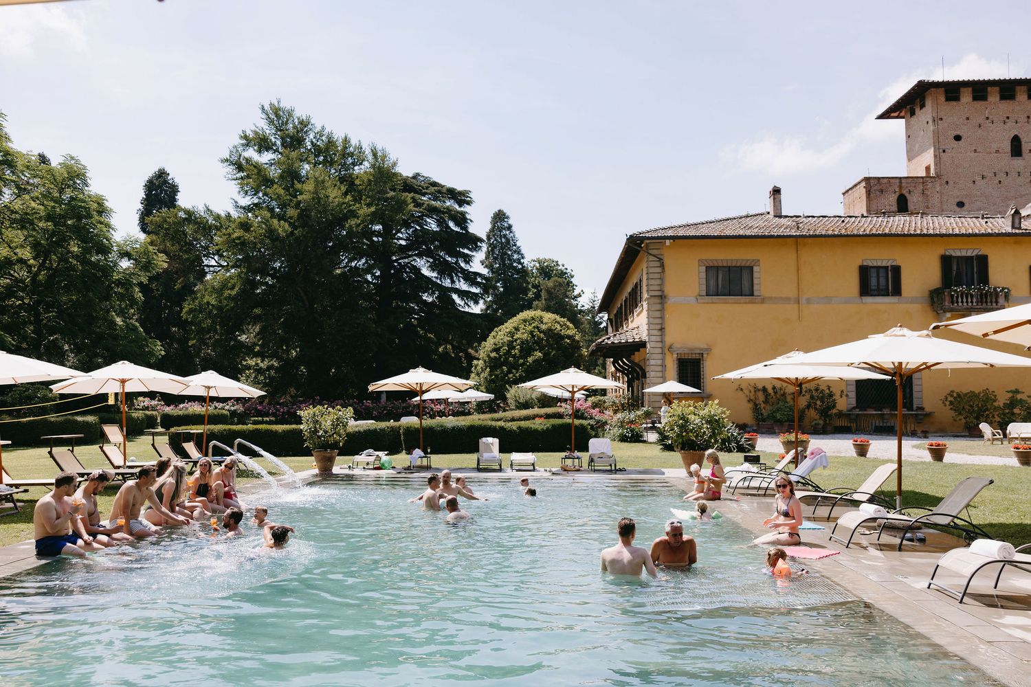 Guests enjoying a luxury swimming pool surrounded by umbrellas at an Italian villa resort.