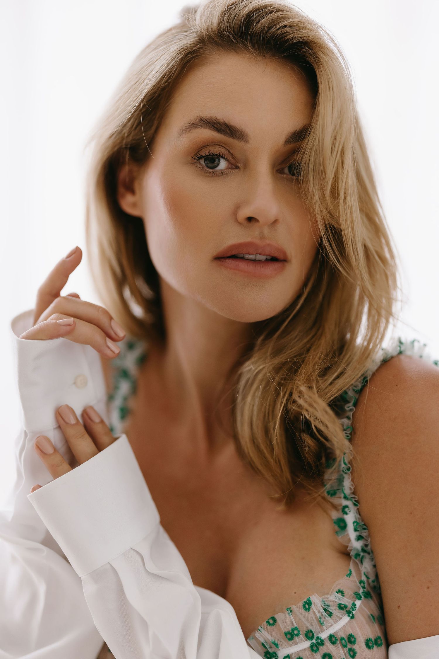 Portrait of woman wearing floral dress and white shirt in soft natural lighting.