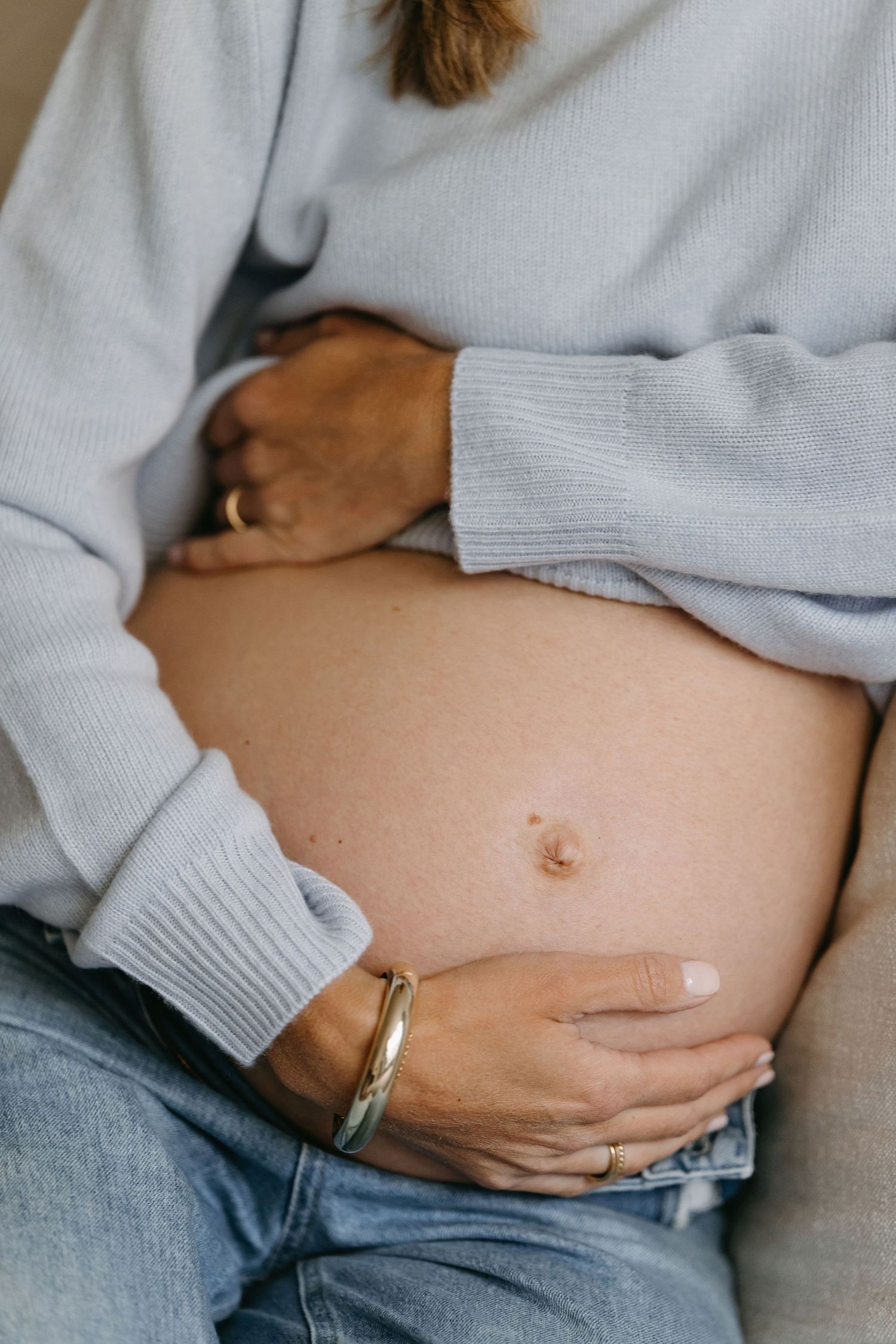Close-up series of pregnant belly in soft sweater and jeans showing wedding ring detail.