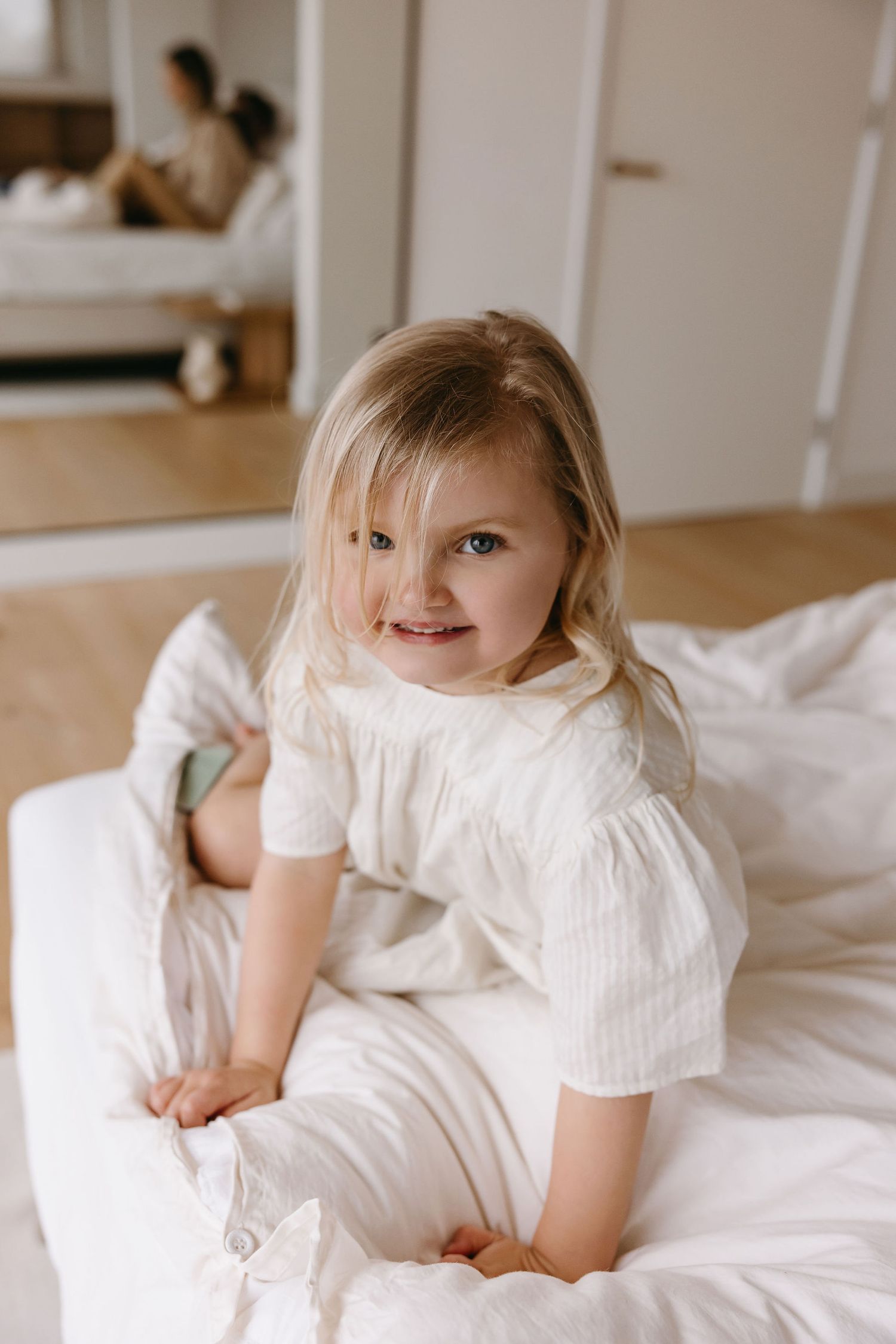 A bright indoor portrait with soft white bedding and natural lighting.