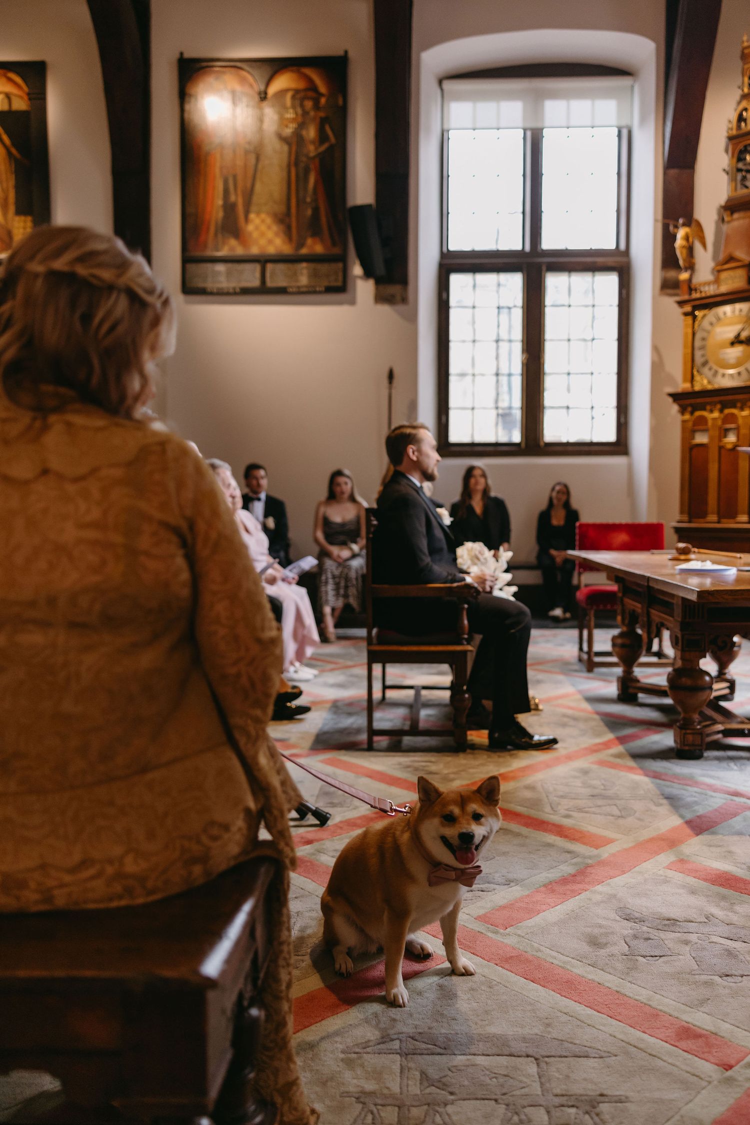 An interior church scene with wooden pews and a corgi sitting in the aisle during a ceremony.
