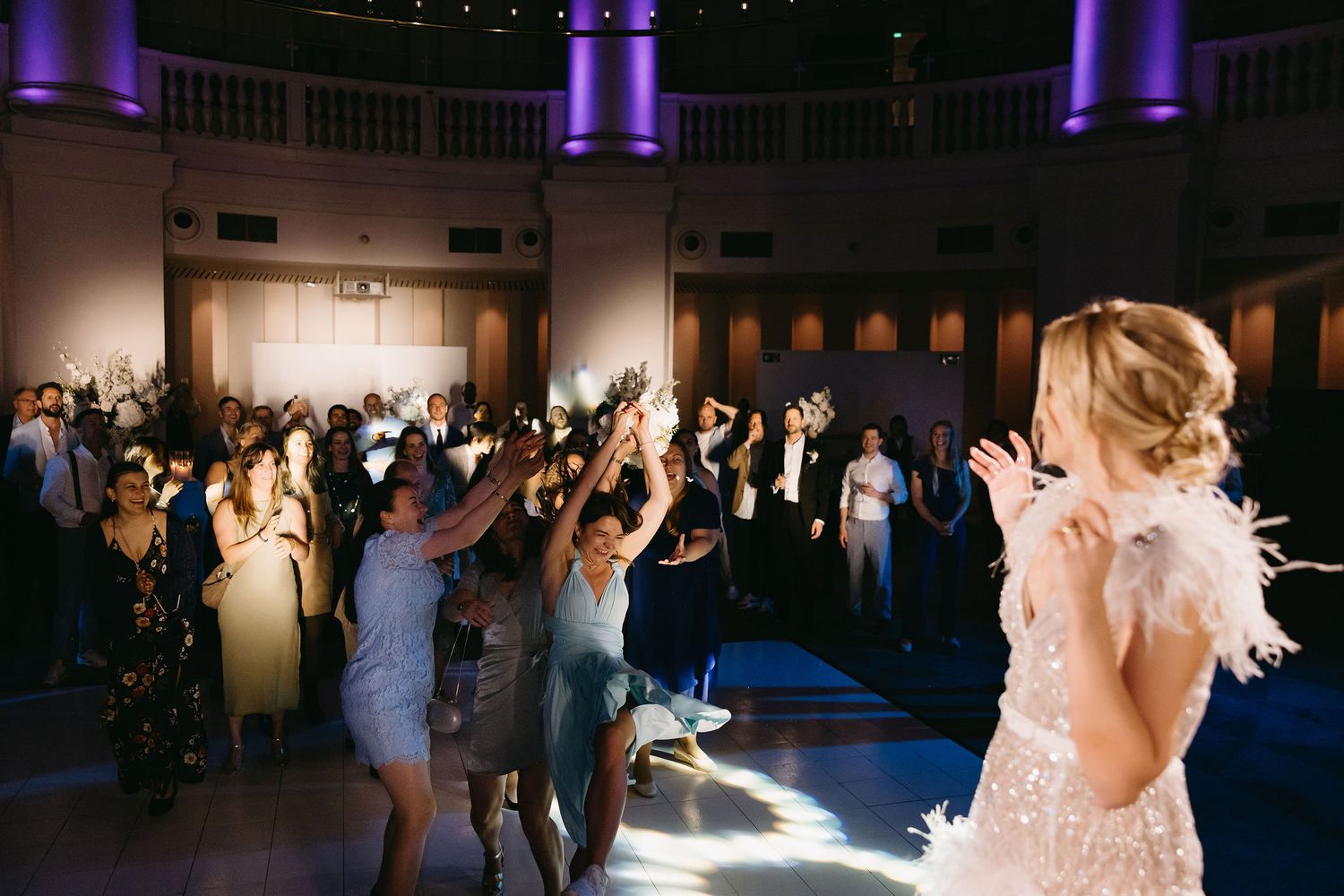 Wedding reception dance floor with purple uplighting and guests dancing in celebration.