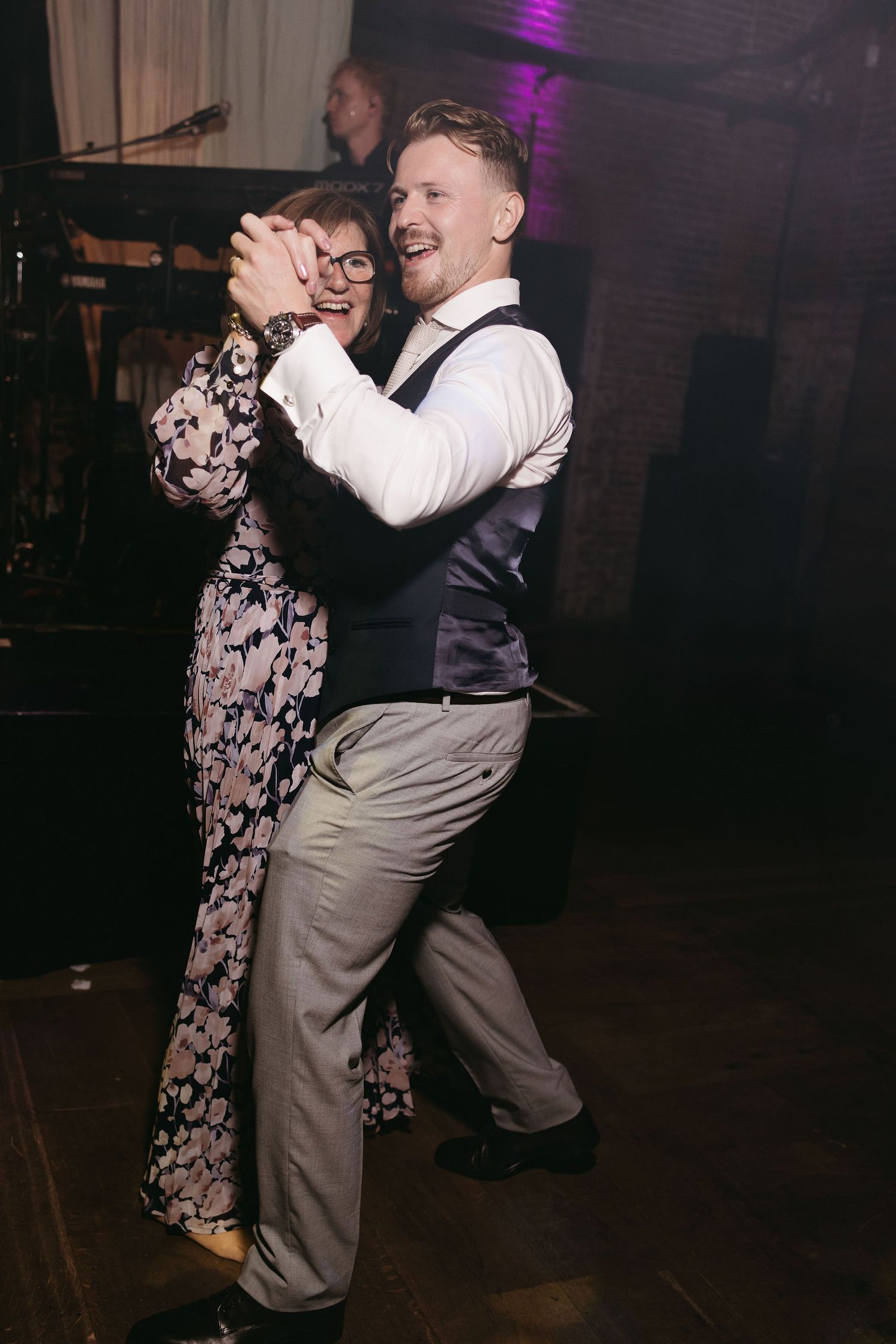 A couple dancing together at a wedding reception in a dimly lit room with purple lighting.