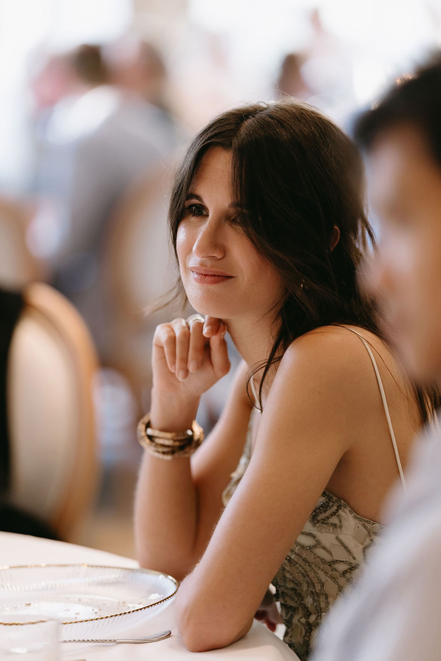 Guest in formal attire at wedding reception rests chin on hand while seated at table.