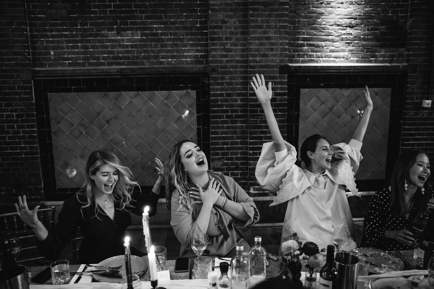 Guests dance and celebrate on a festive dance floor at a wedding reception with brick walls and mood lighting.