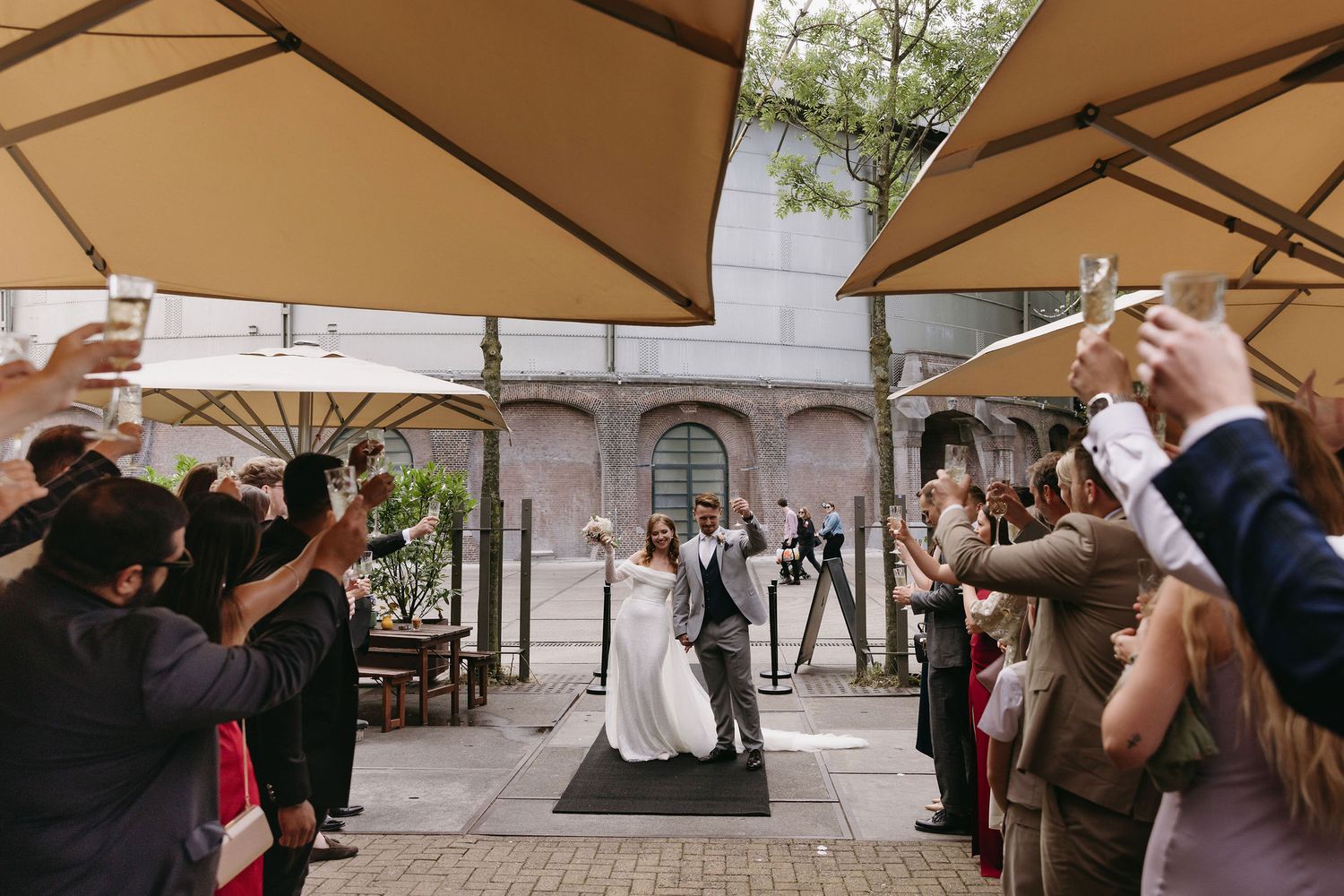 Wedding celebration under beige umbrellas in an outdoor courtyard setting.