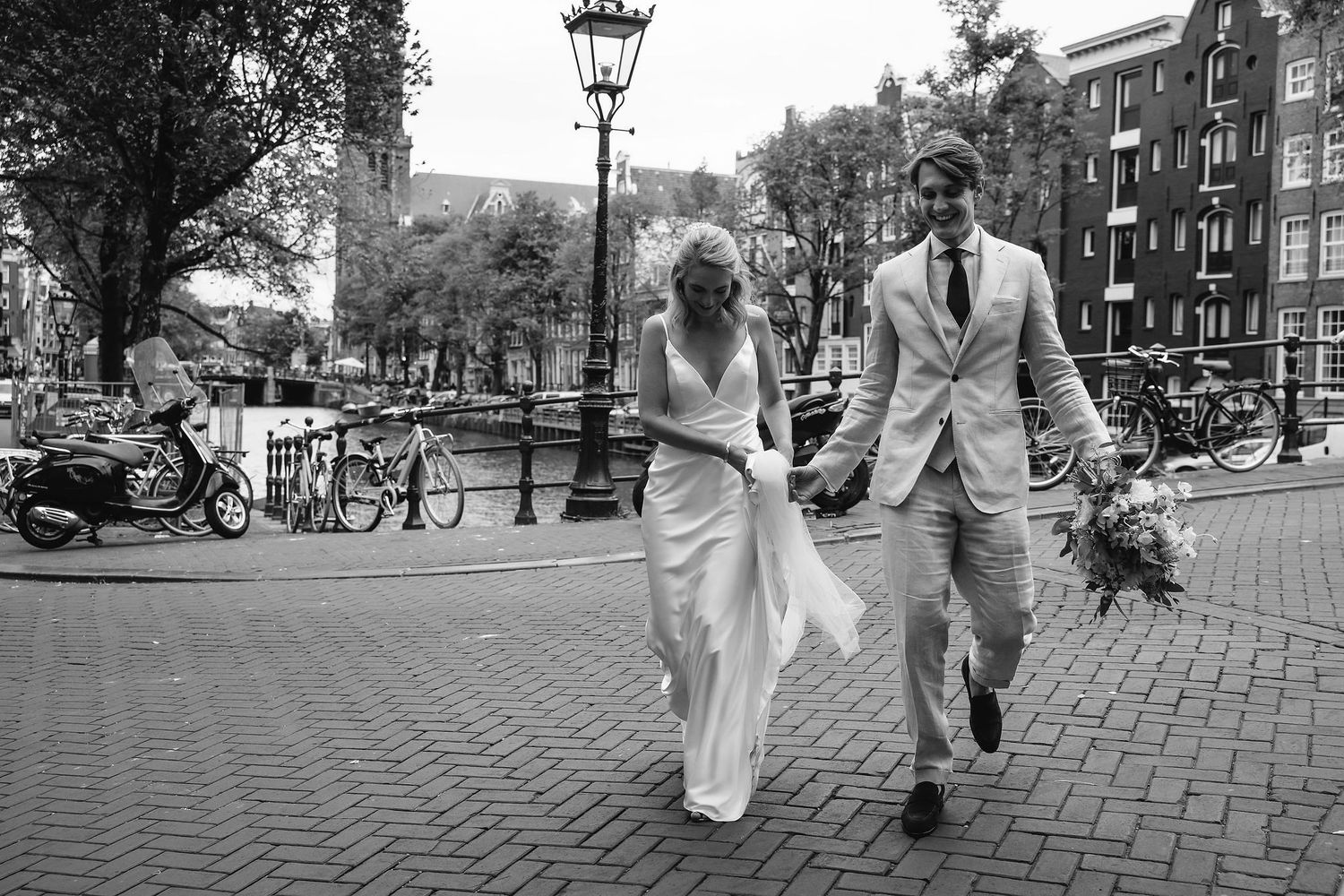Black and white photo of couple walking hand in hand on cobblestone street in Amsterdam.