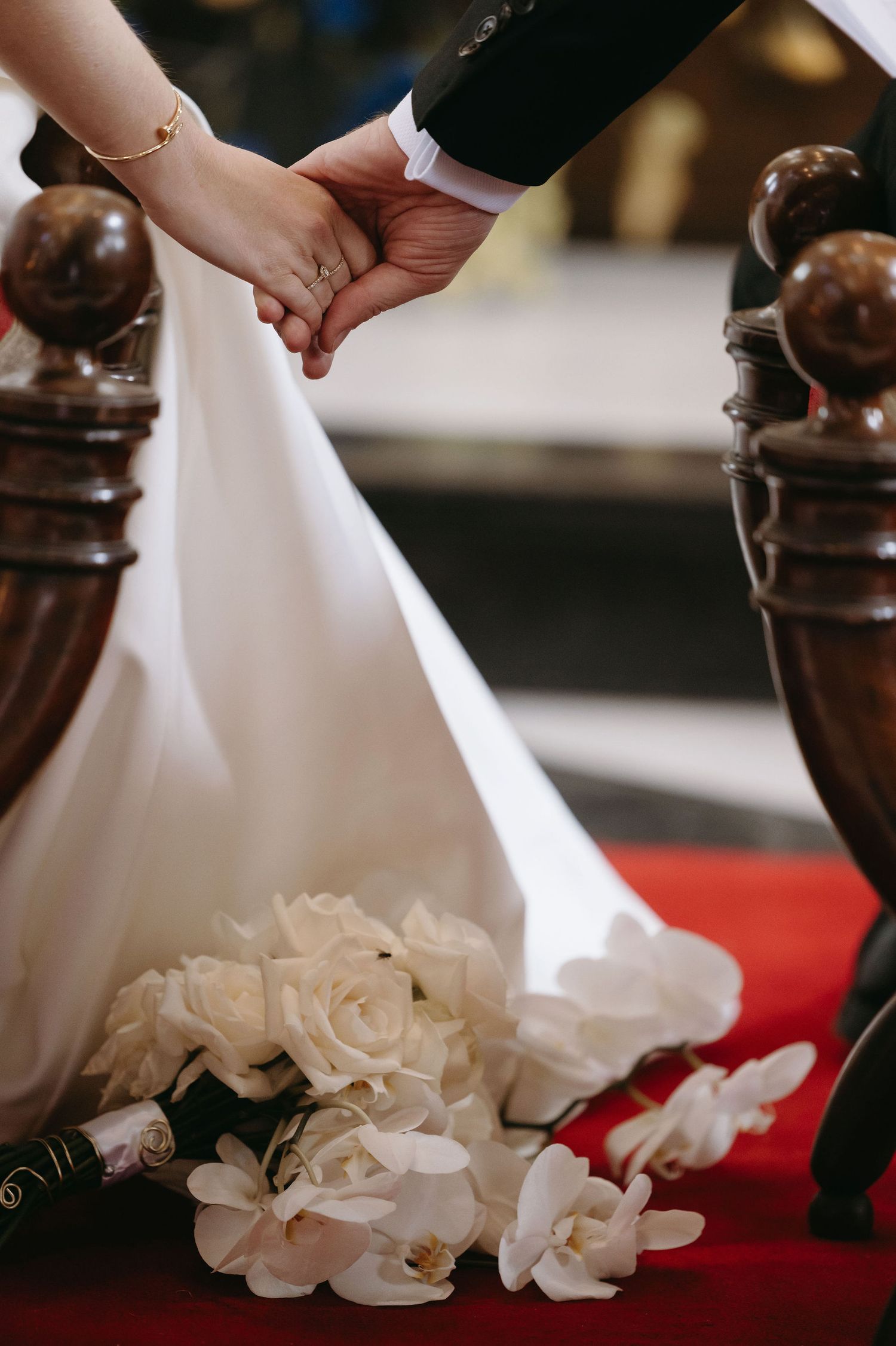 Two hands clasped together over white wedding flowers and red fabric during a ceremony.
