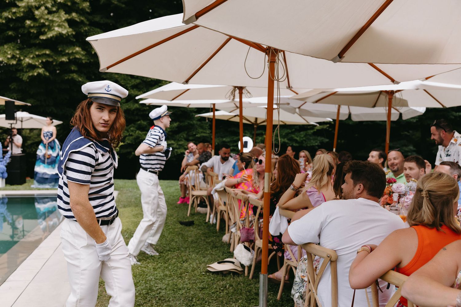 Guests enjoying a poolside party under white umbrellas on a sunny day.