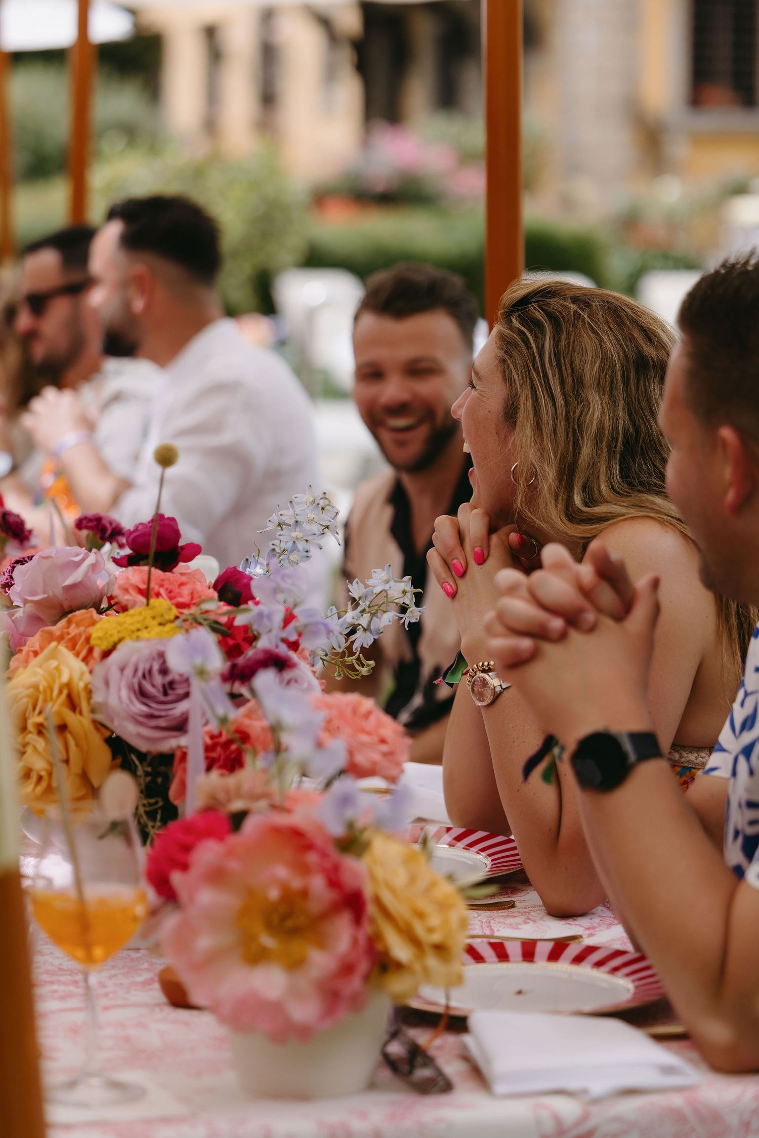Wedding reception table decorated with vibrant floral centerpieces of pink, orange and yellow roses.