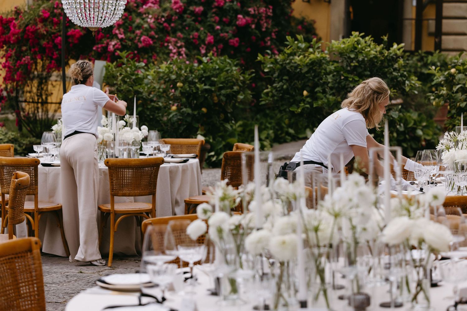 Event staff preparing elegant table settings with white floral centerpieces outdoors.